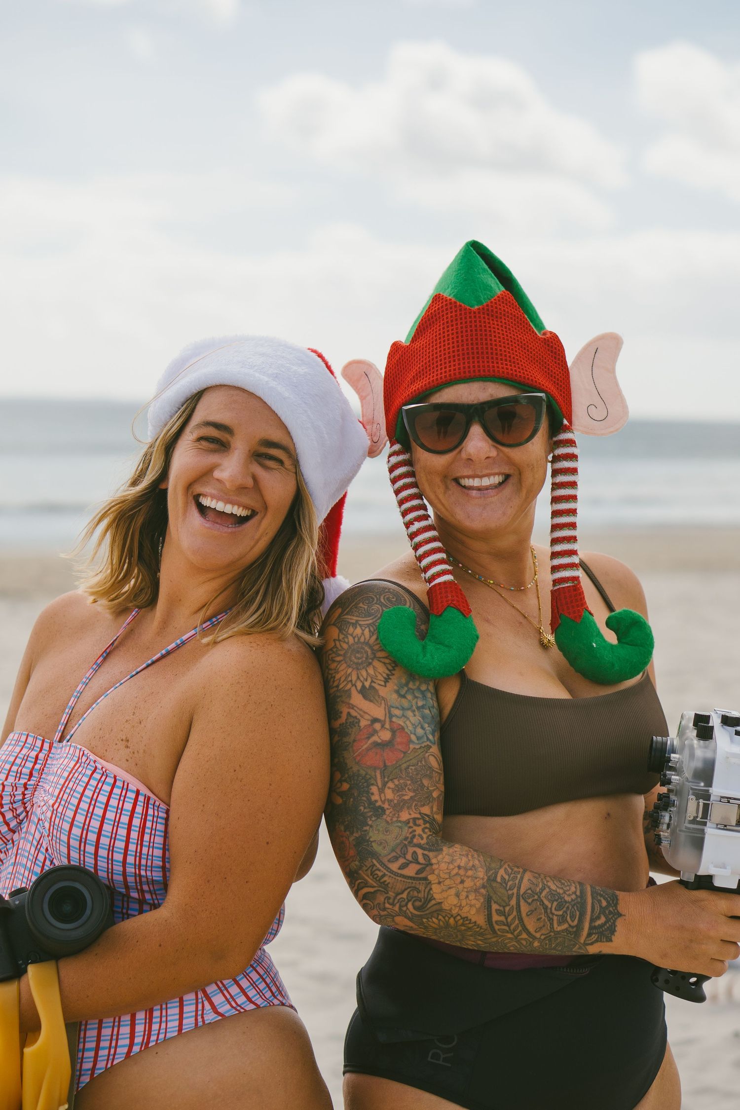 Friends wearing holiday hats and festive attire posing together on sunny beach.
