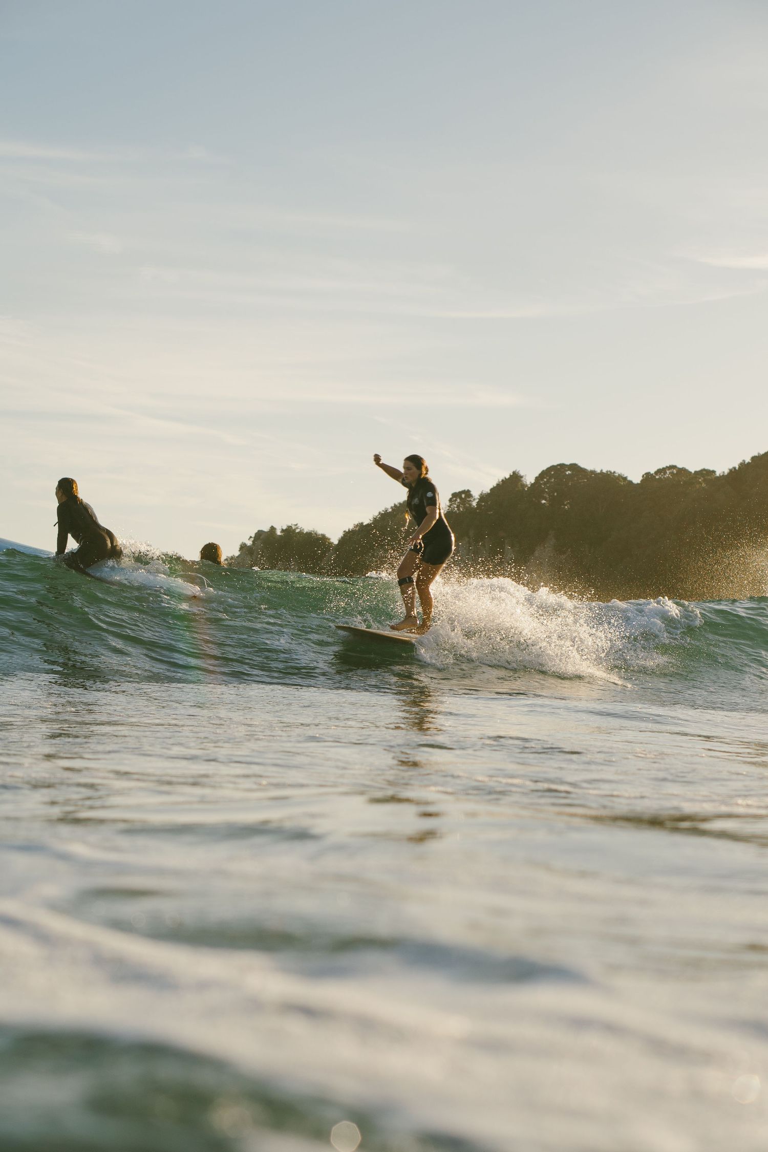 Multiple surfers riding waves at sunset with coastal landscape.