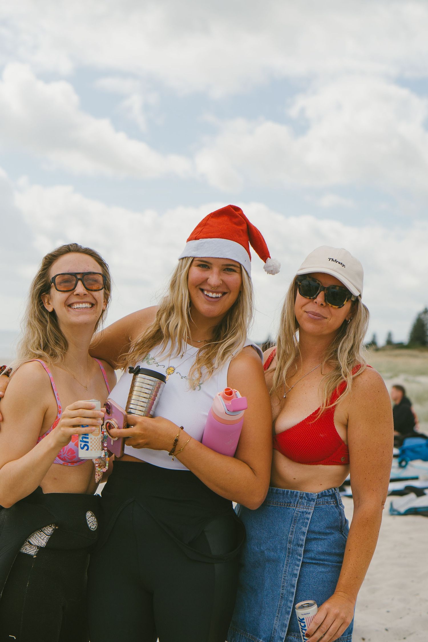 Friends in beachwear and Santa hats enjoy drinks together on sunny beach.