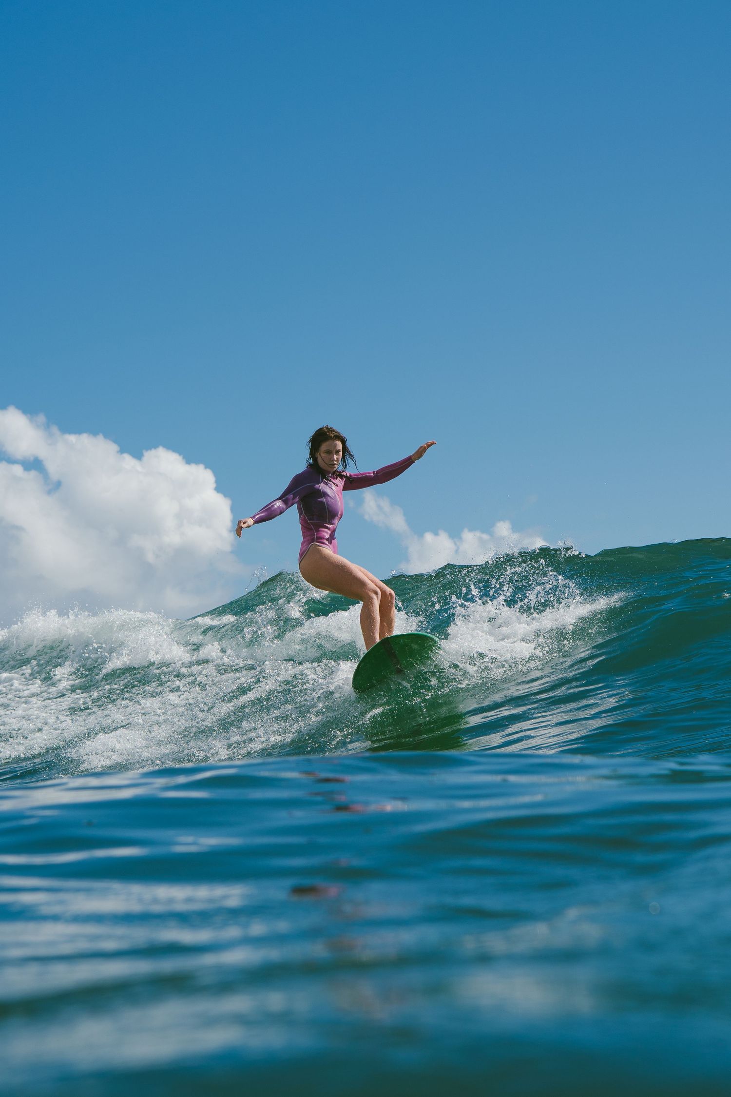 Surfer in purple swimsuit performs dynamic maneuver on rolling ocean wave.