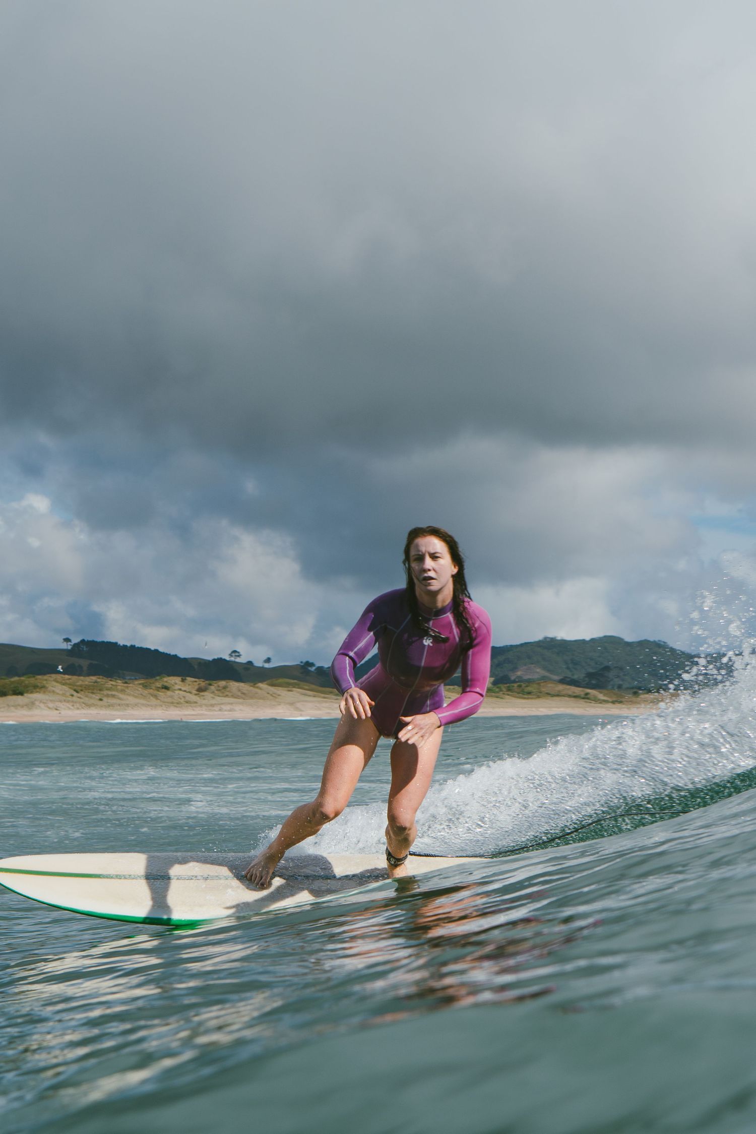Surfer rides wave in purple wetsuit against stormy coastal backdrop.