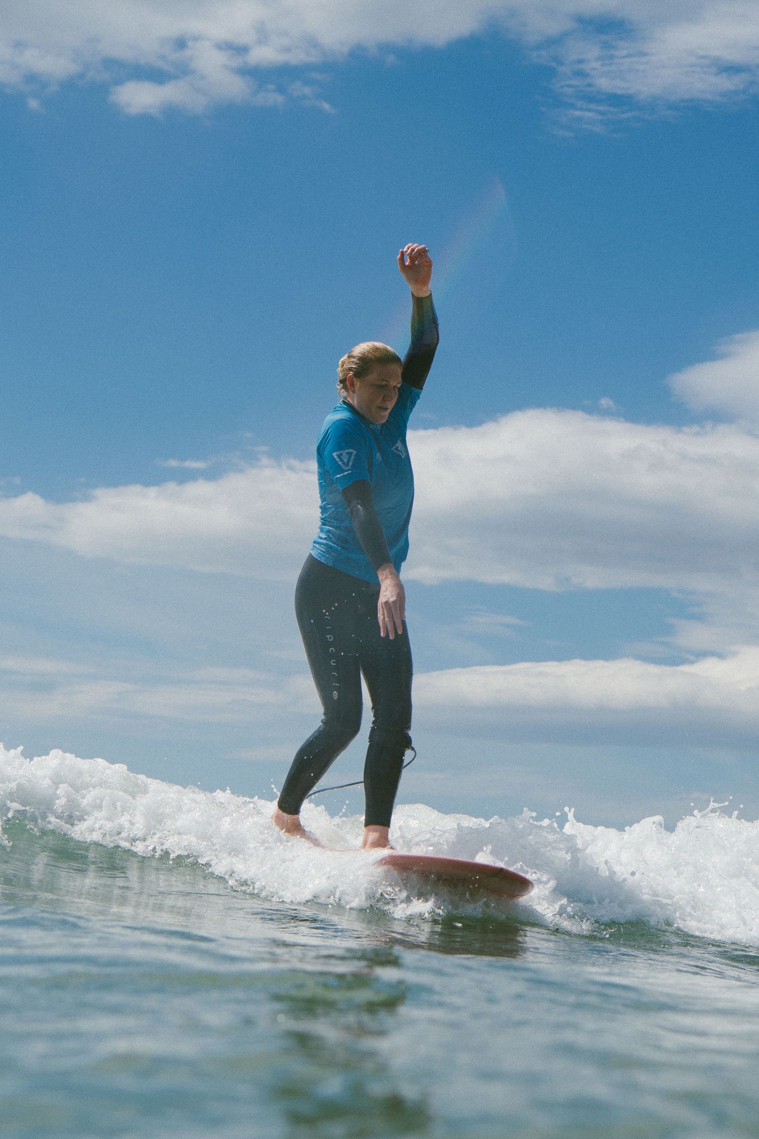 Surfer rides a wave on a sunny day with blue skies and white clouds in the background.