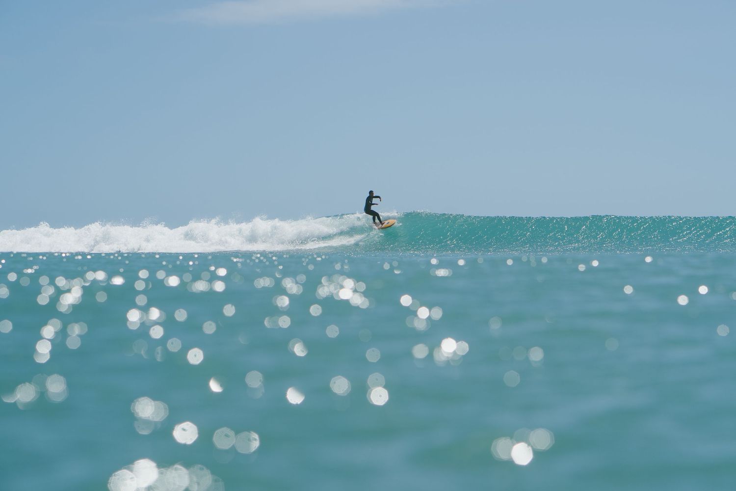Surfer rides along the crest of a breaking wave in sparkling turquoise waters.
