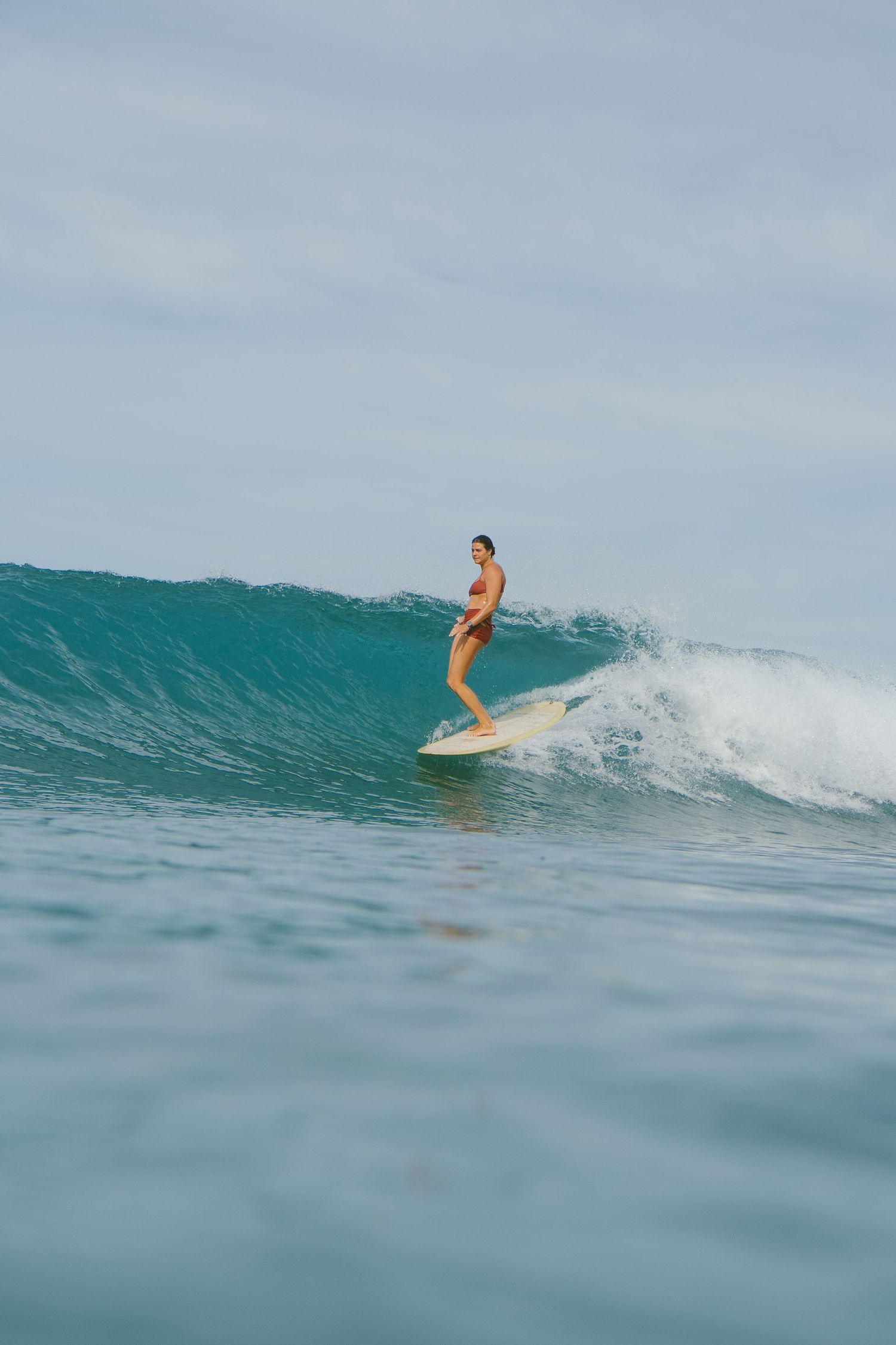 A surfer in a yellow bikini rides a turquoise wave on a longboard in clear ocean waters.