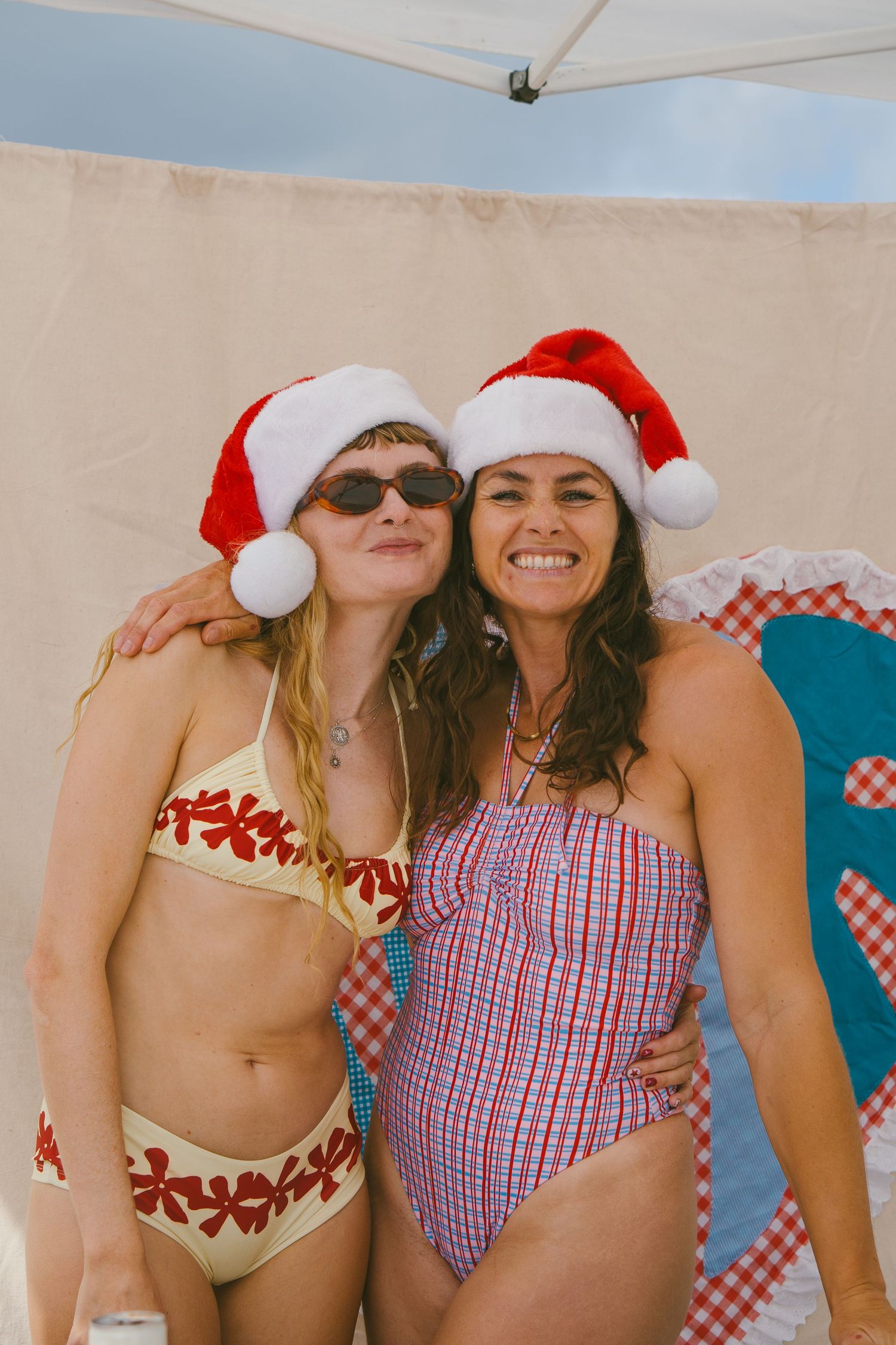 People wearing Santa hats pose together at the beach in matching red and white swimwear and outfits.