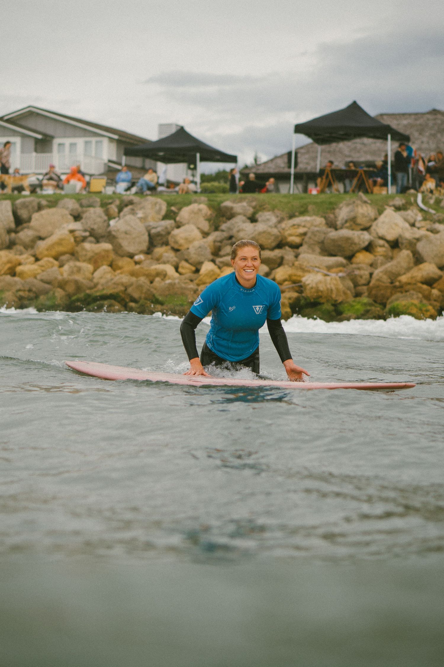 Surfer in blue wetsuit paddling through ocean waves near rocky coastline.