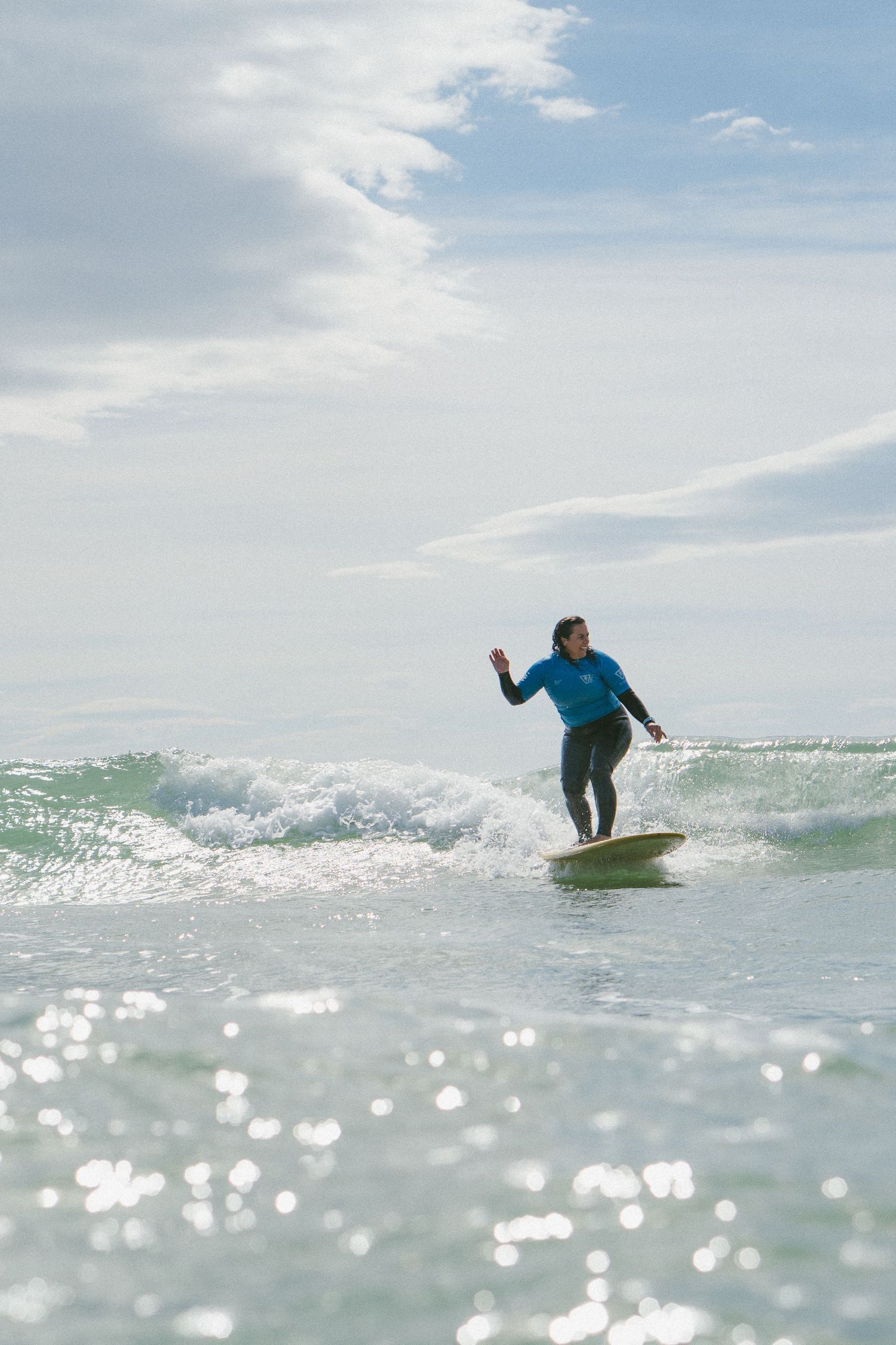Surfer riding wave in blue wetsuit with glittering ocean surface.