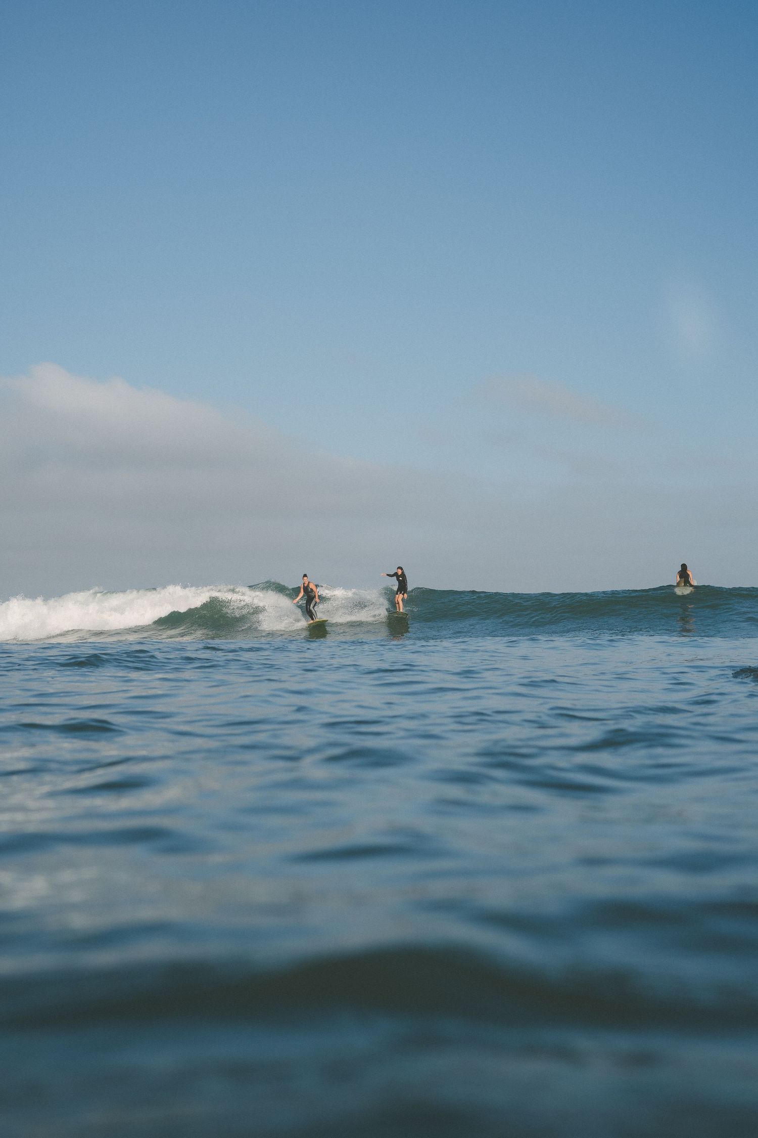 Wide angle ocean view with distant surfers catching waves on the horizon.