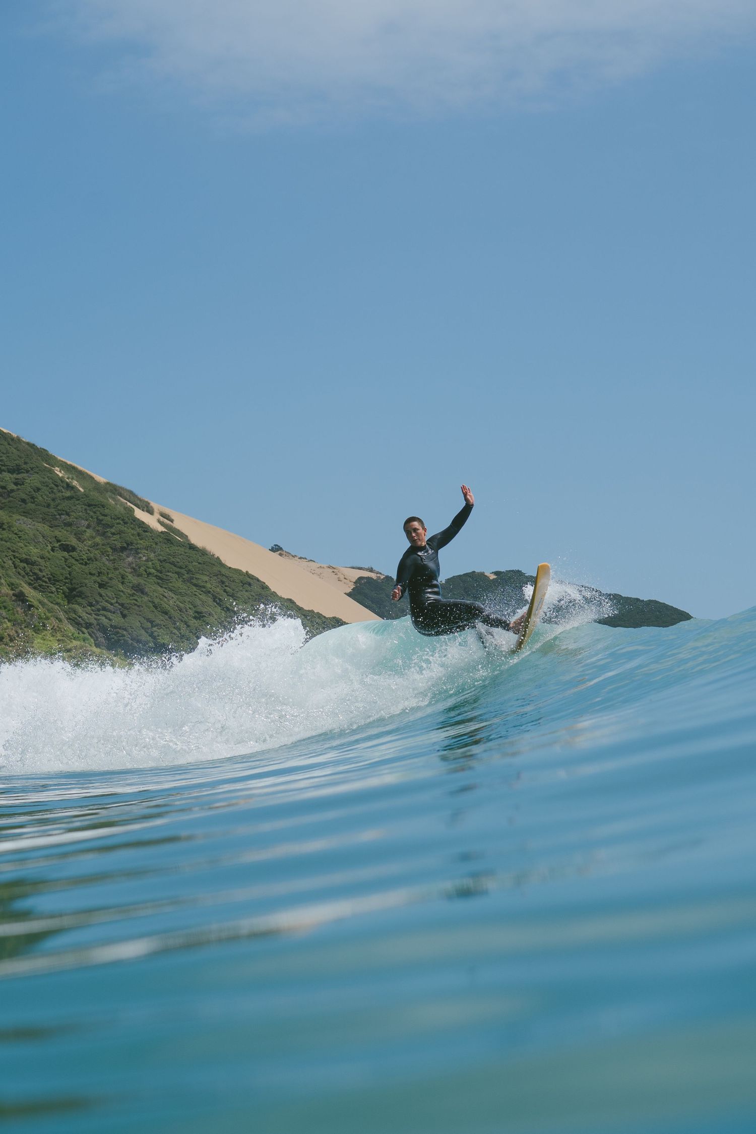 Surfer performs dynamic aerial maneuver against backdrop of coastal landscape.