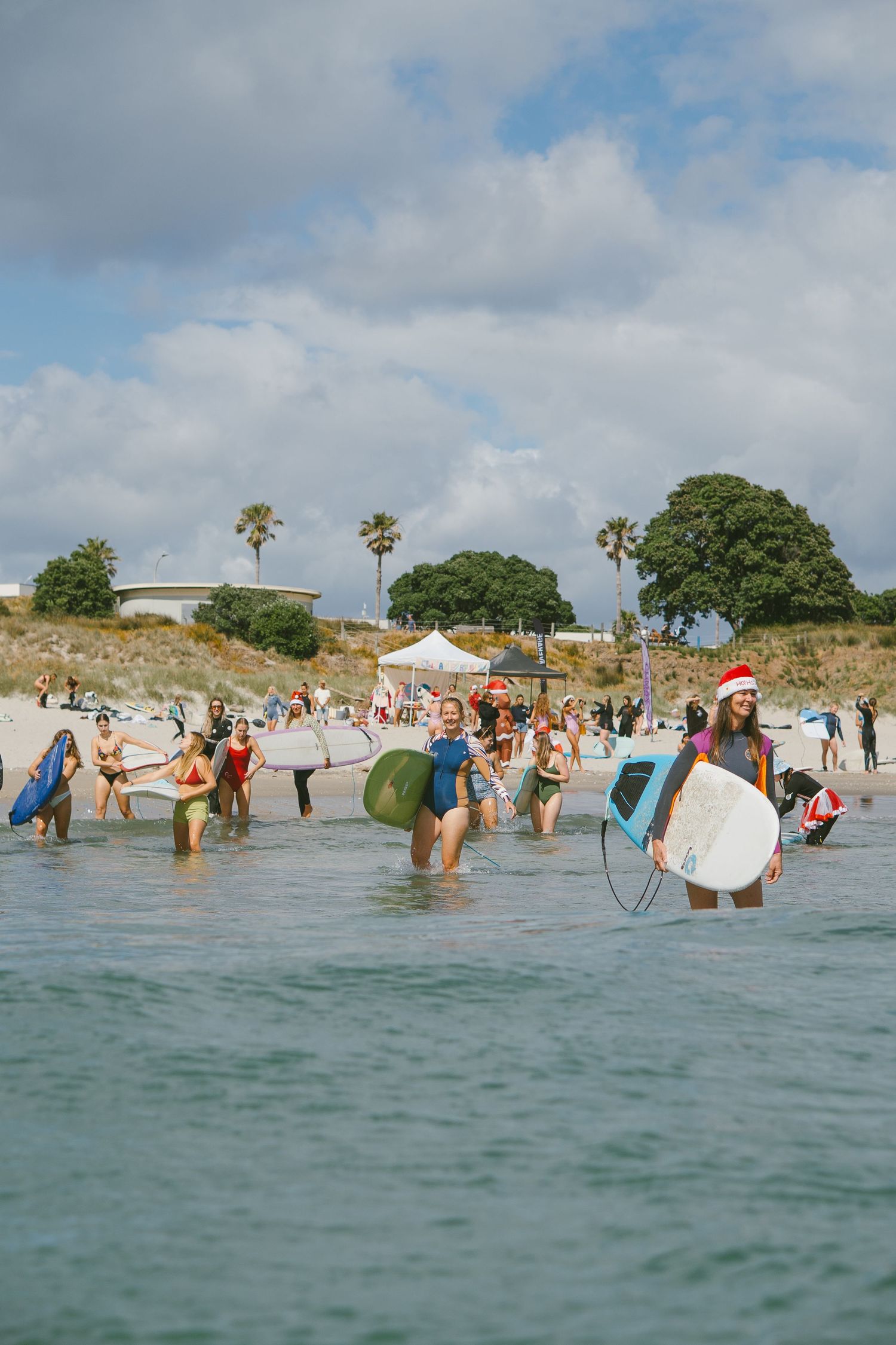 Group of surfers gathered in shallow ocean water with surfboards during a holiday event.