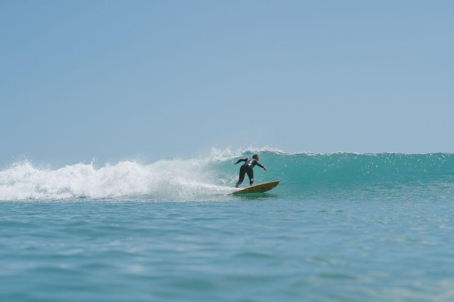 Surfer rides a turquoise wave on a bright sunny day, performing aerial maneuvers in crystal clear waters.