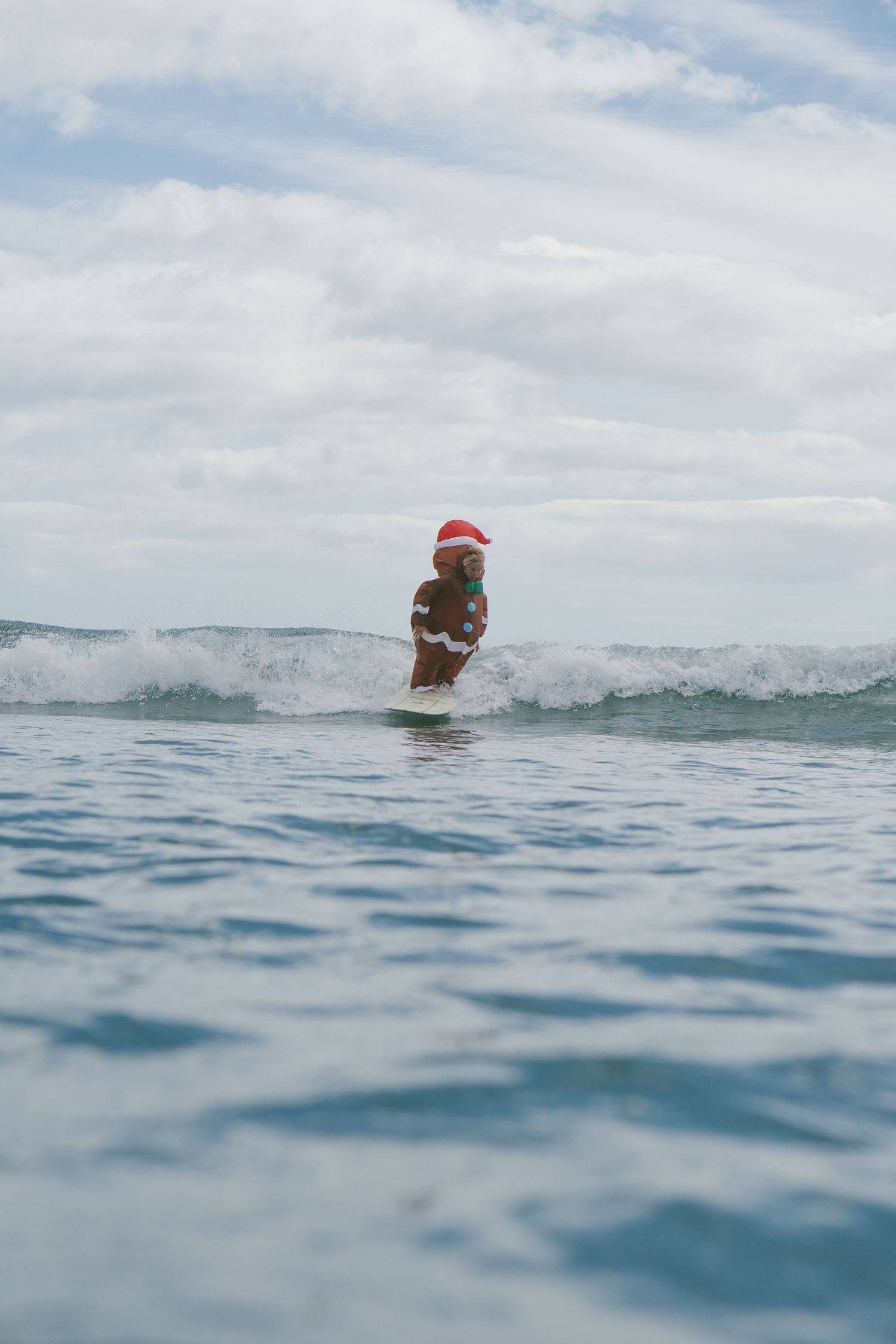 Santa hat wearing surfer visible in distance among ocean waves.