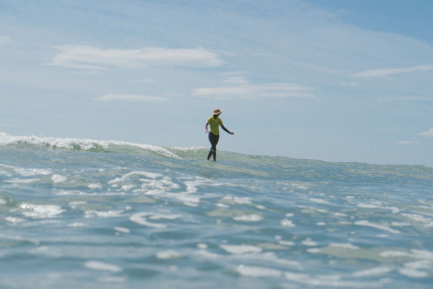 Distant surfer visible on ocean horizon under bright blue sky.