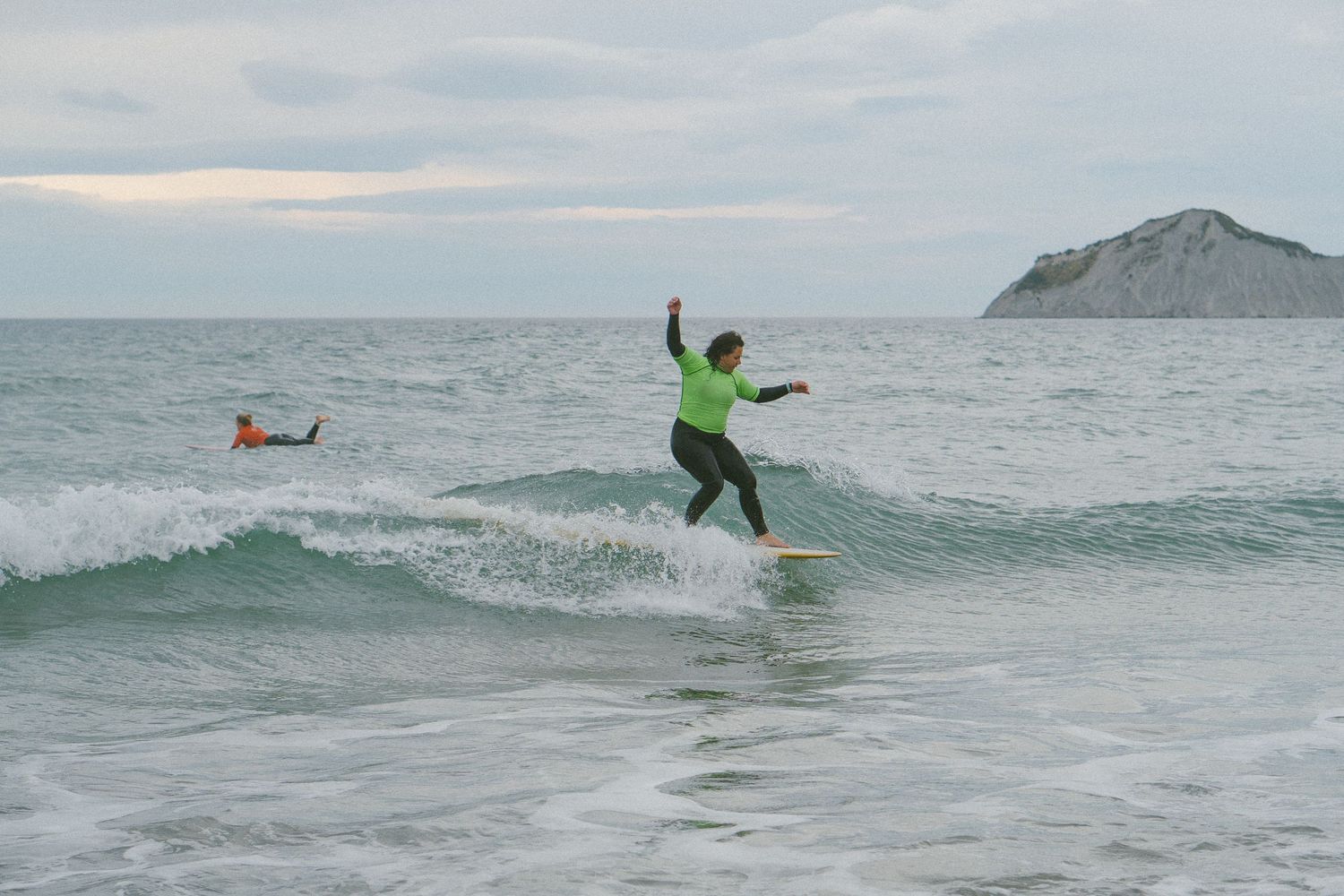 Surfer catching waves at a scenic coastal beach with mountains in background.