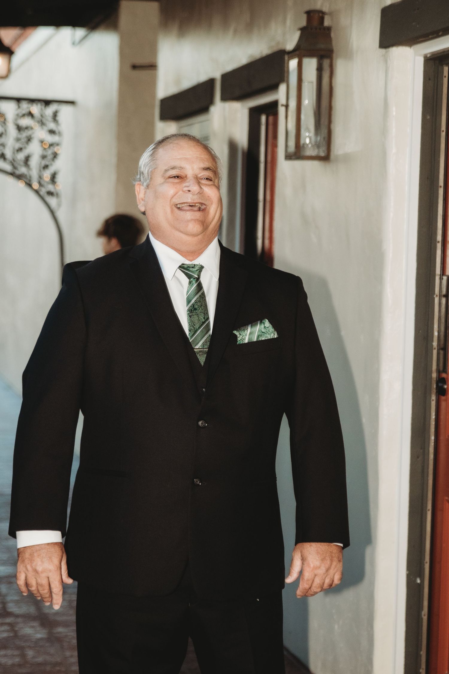 A formal portrait of a gentleman in a black suit with green tie and pocket square.