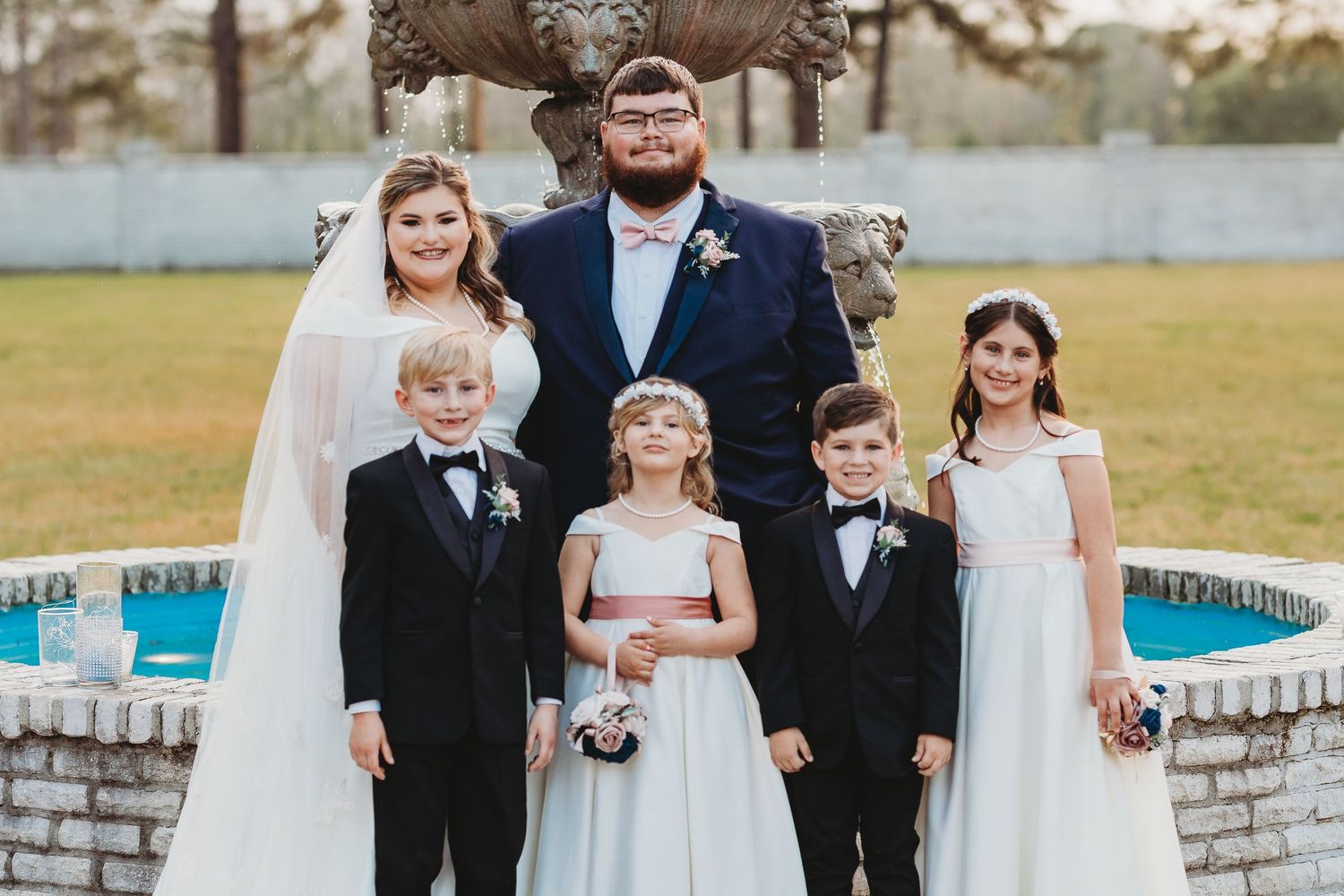 Wedding party members gather for group photos near a decorative stone fountain.