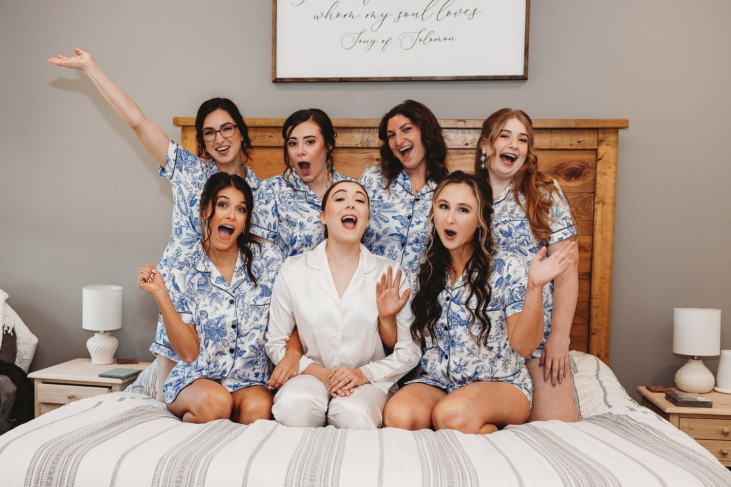 Bridal party in matching floral robes having fun on bed during wedding preparations.