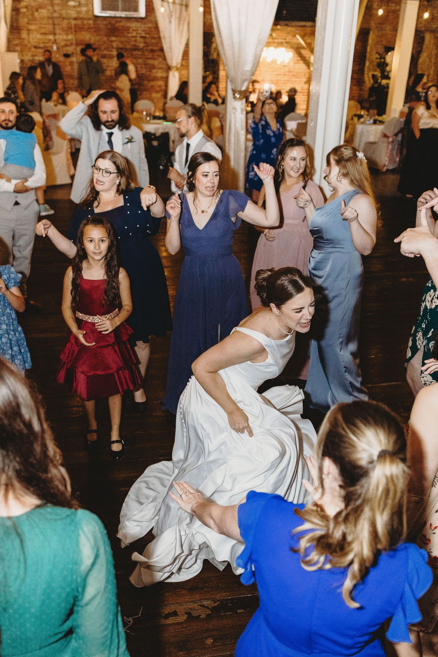 Wedding celebration showing guests dancing energetically in colorful attire at an indoor reception.