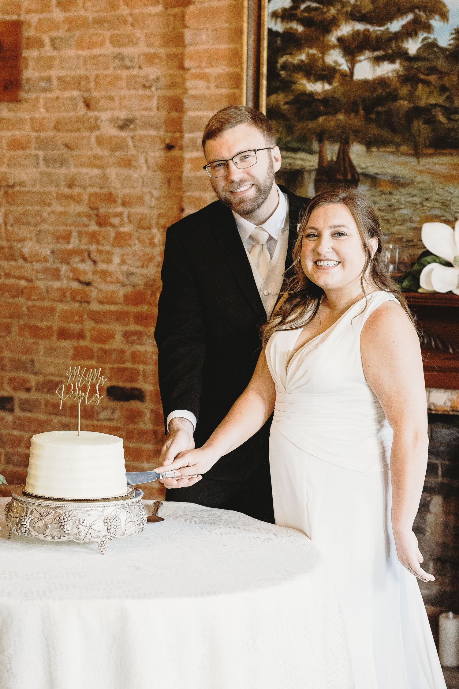 Wedding couple cutting their elegant white cake with silver details.