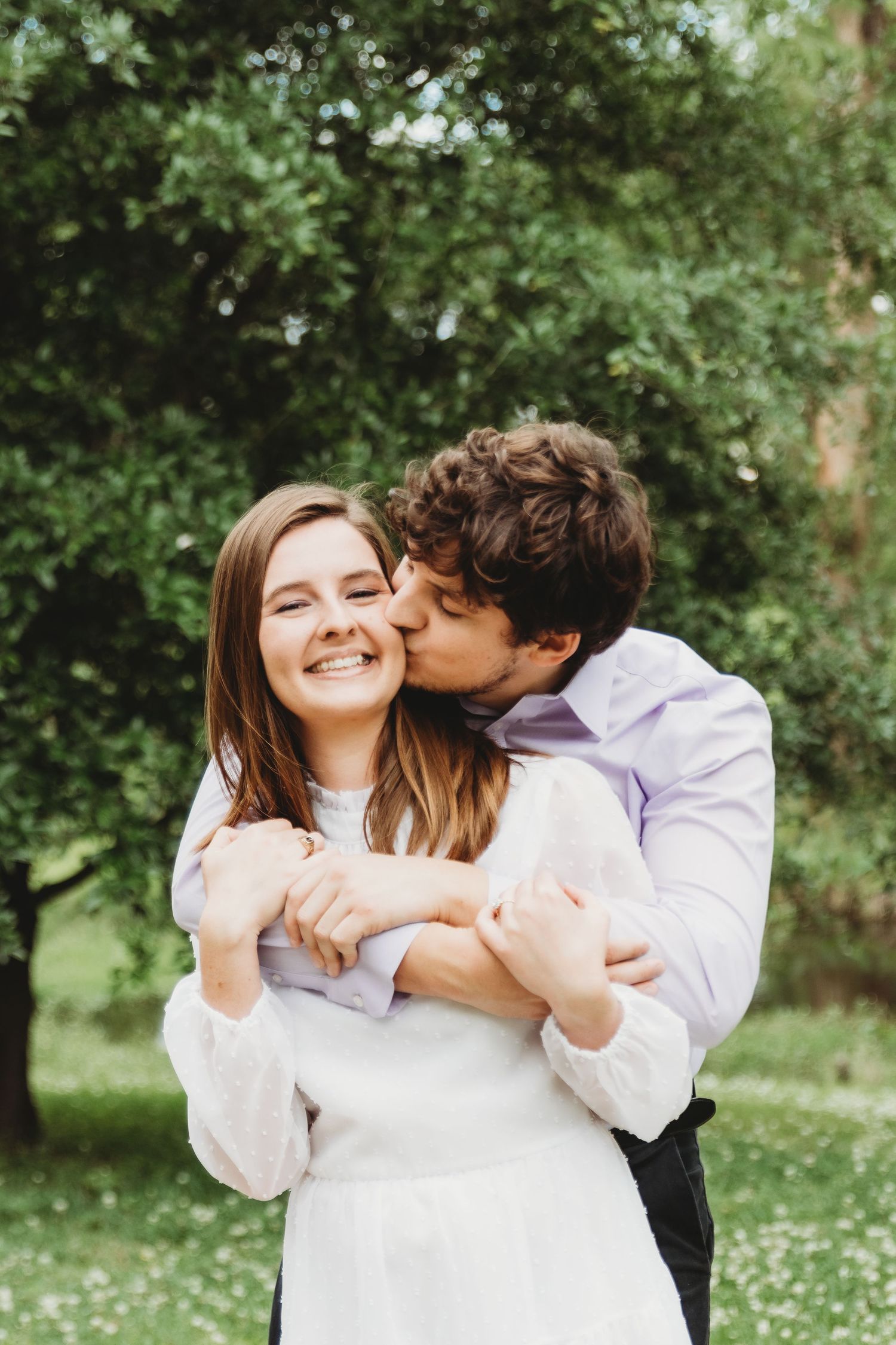 A couple laughs together in a sunny field with white flowers.