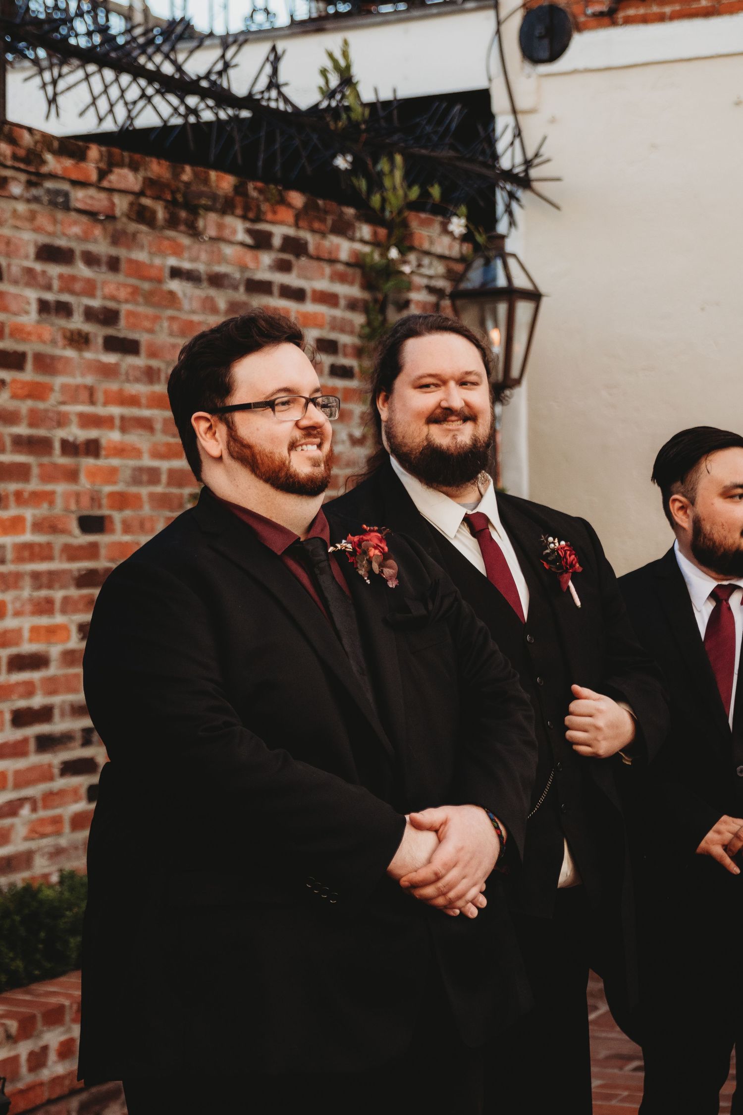 Groomsmen in black suits and red ties share candid laughter during wedding festivities.