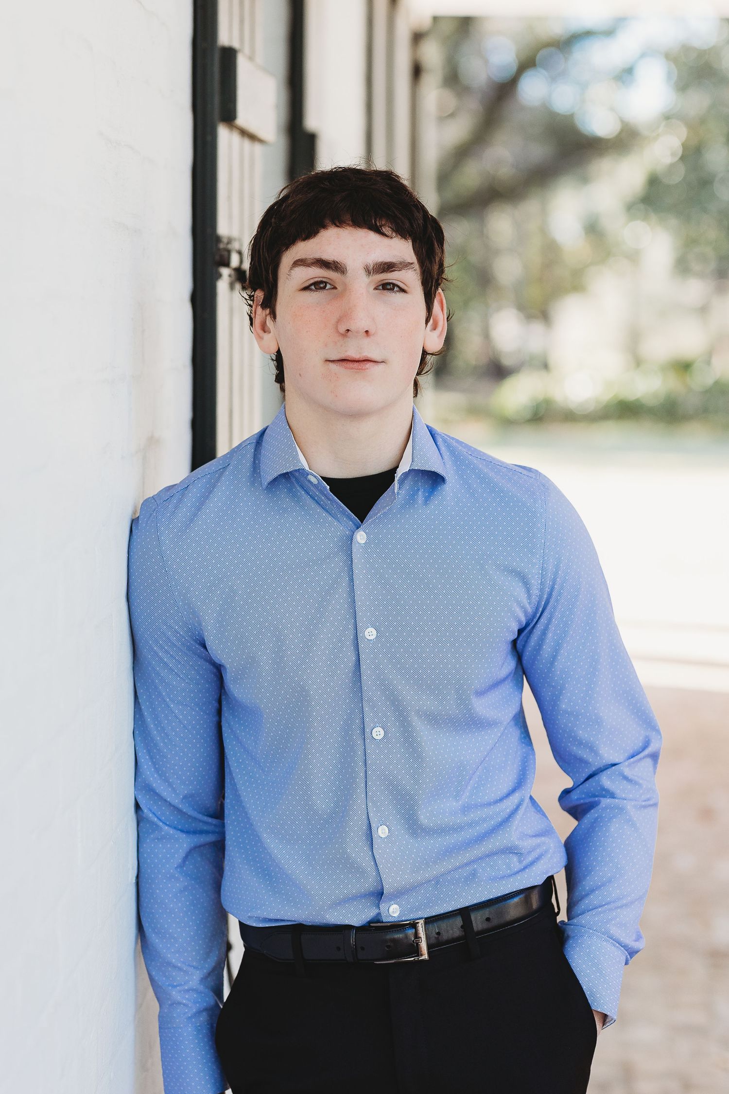 A professional headshot of someone wearing a blue collared shirt against a white wall.