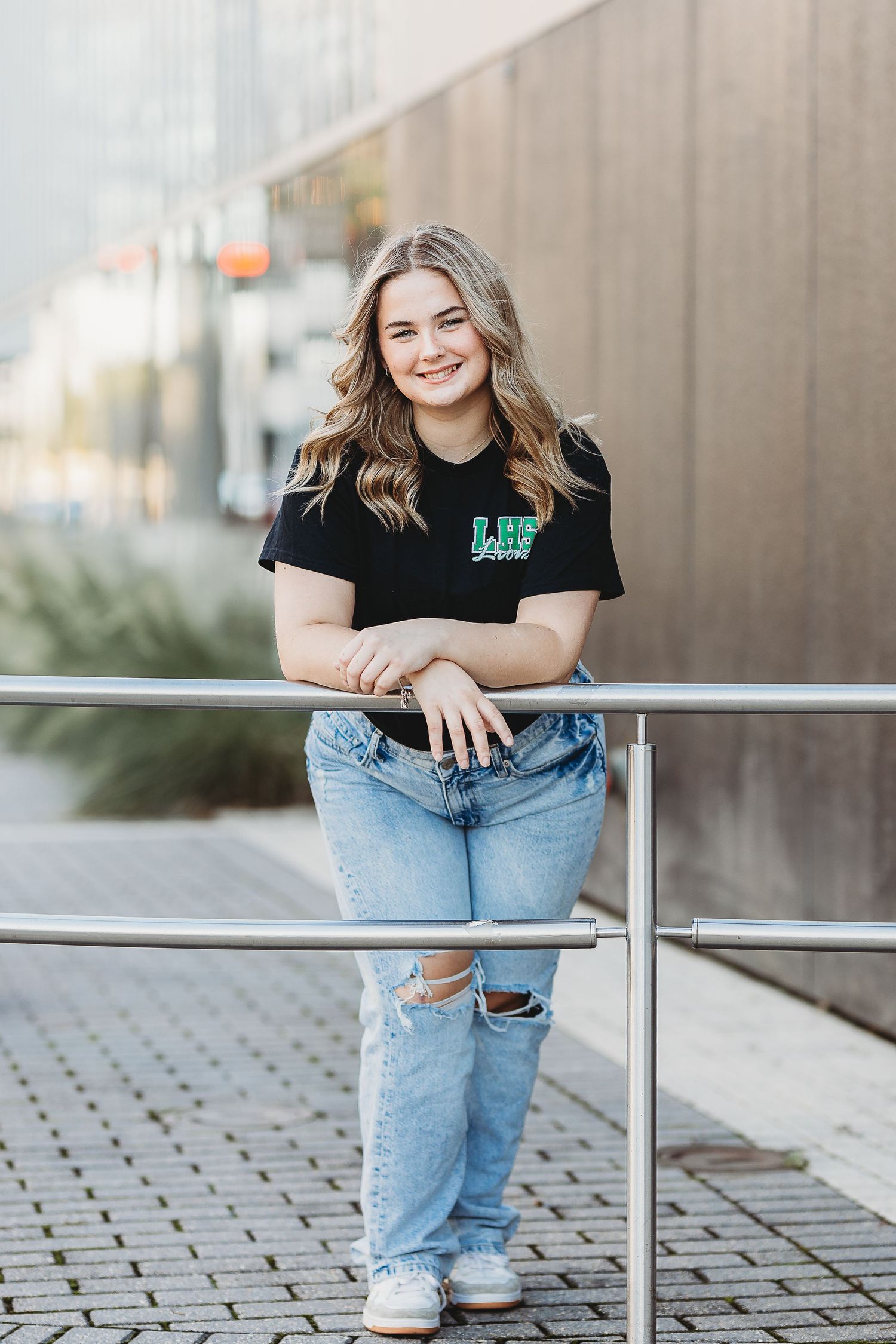 Urban style portrait with distressed denim and black top against modern architecture.