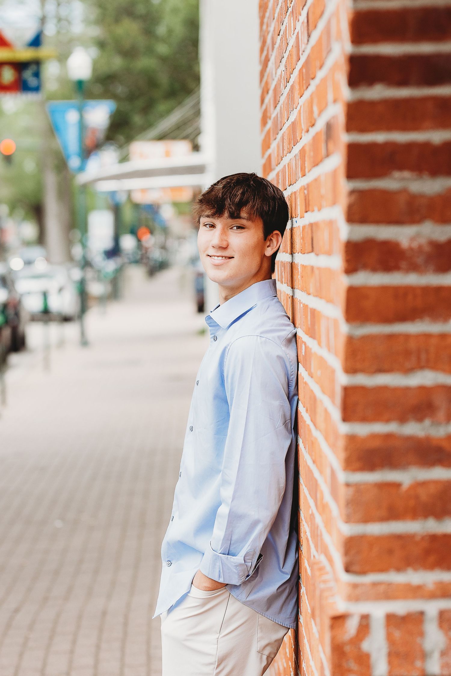 Casual portrait against brick wall with urban sidewalk and street in background.