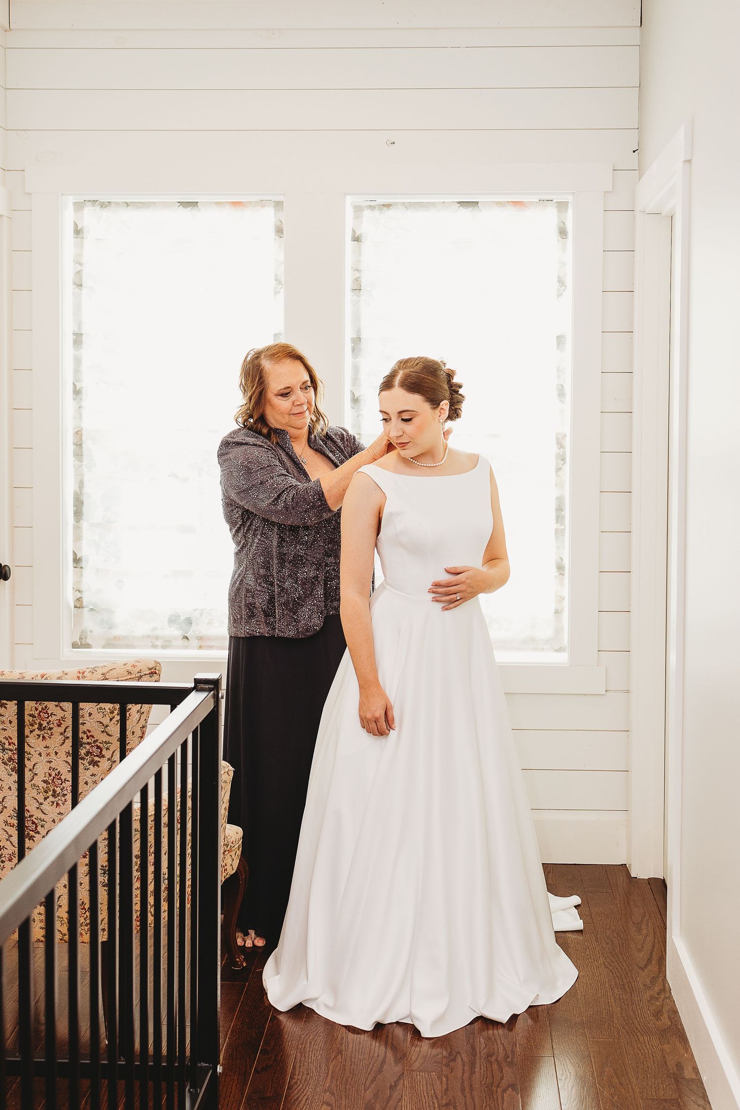 Wedding party members share joyful moments in a bright indoor hallway with white walls and wooden floors.