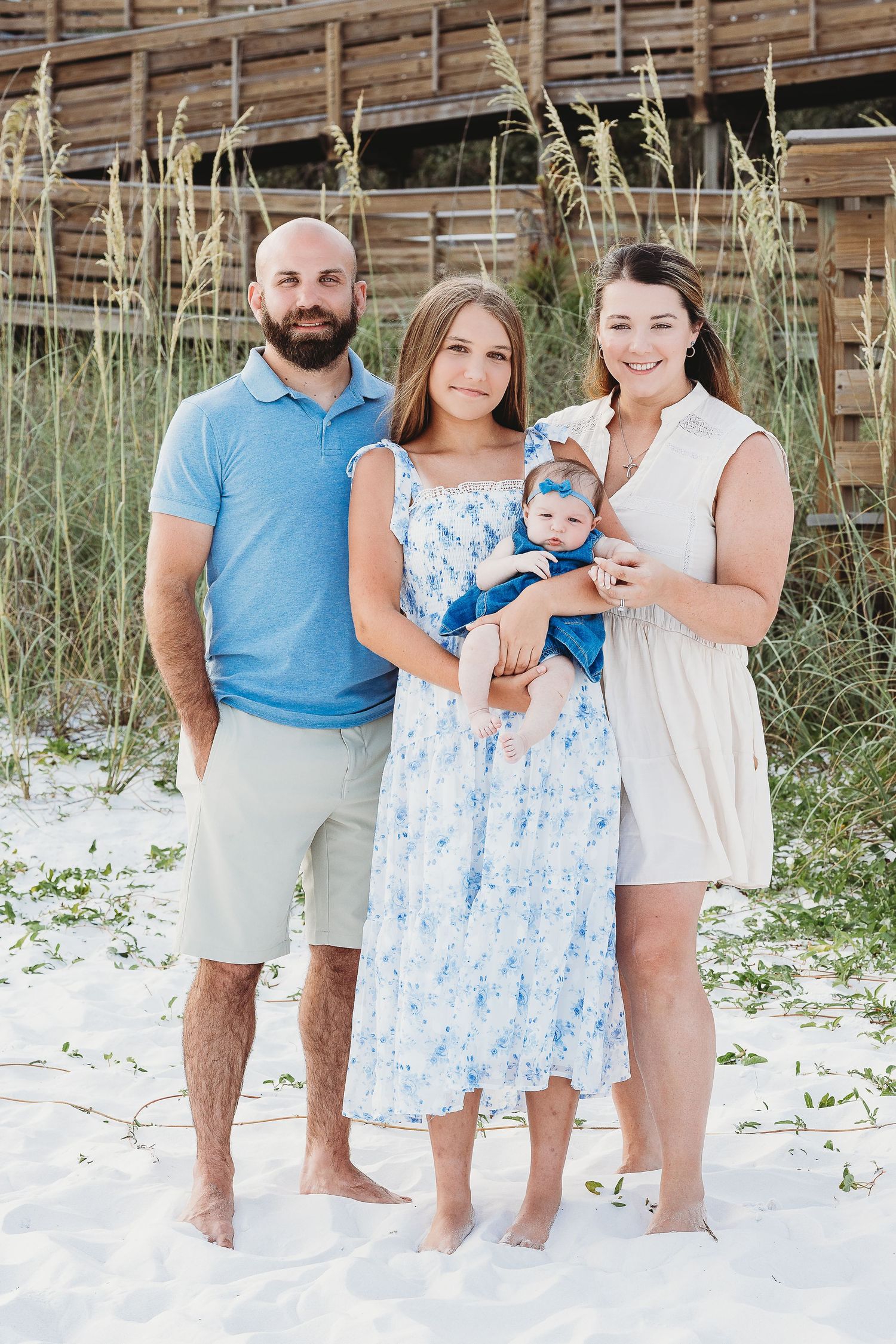 Family beach portrait session with coordinating blue and white outfits on white sand.