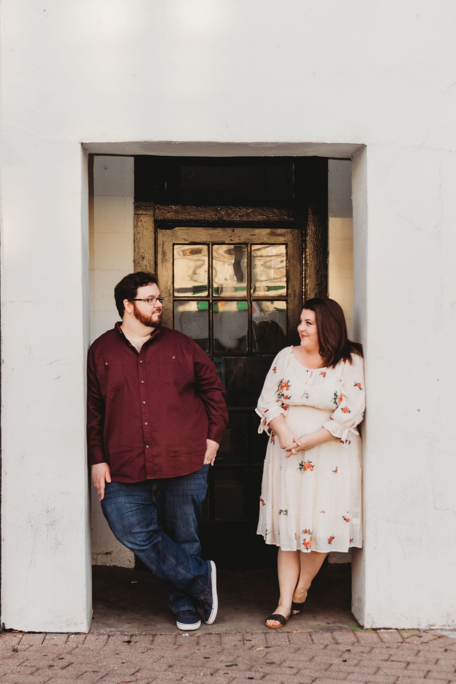 A couple shares candid moments in front of a white building with archways.