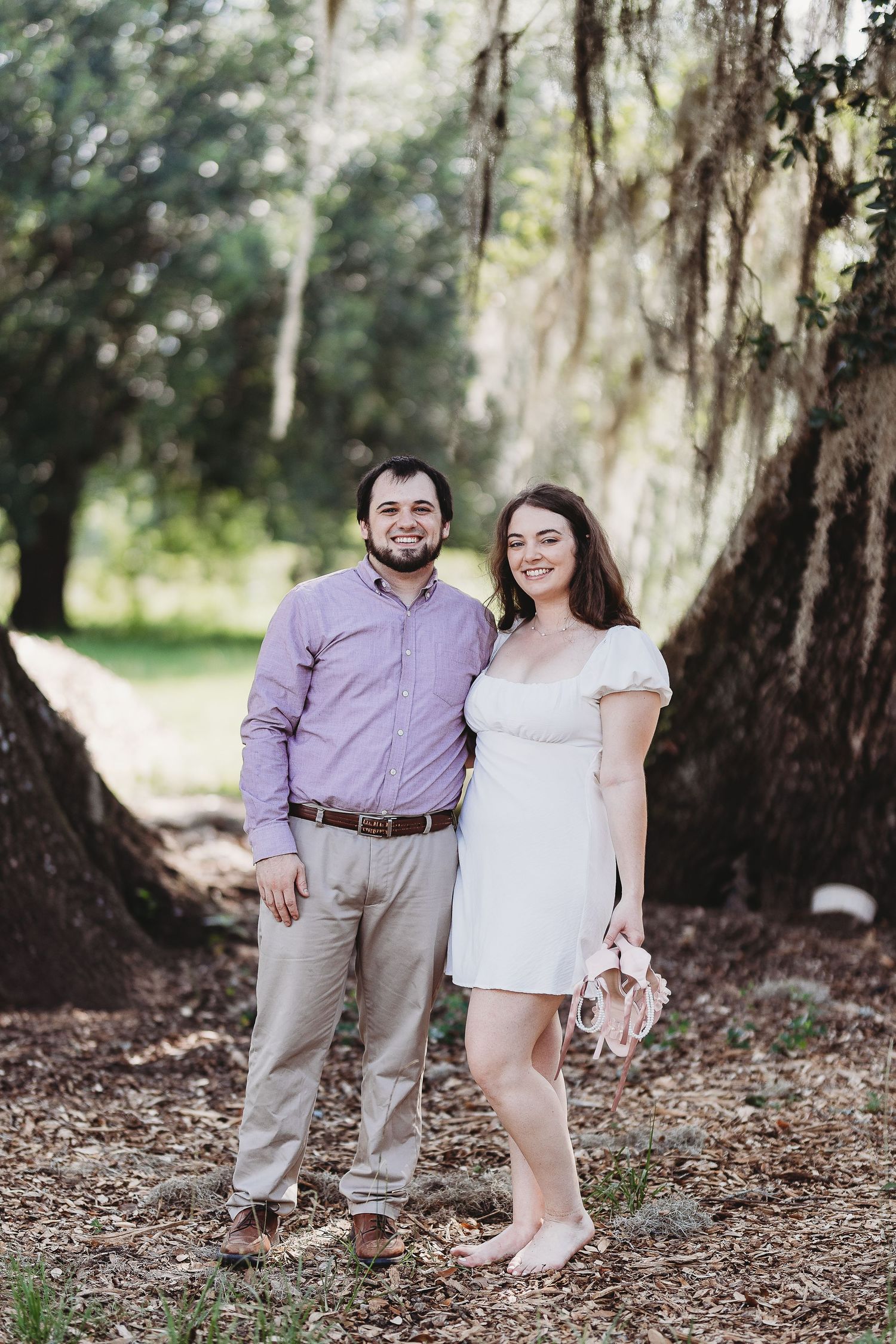 A couple poses together among trees with hanging Spanish moss in a natural outdoor setting.
