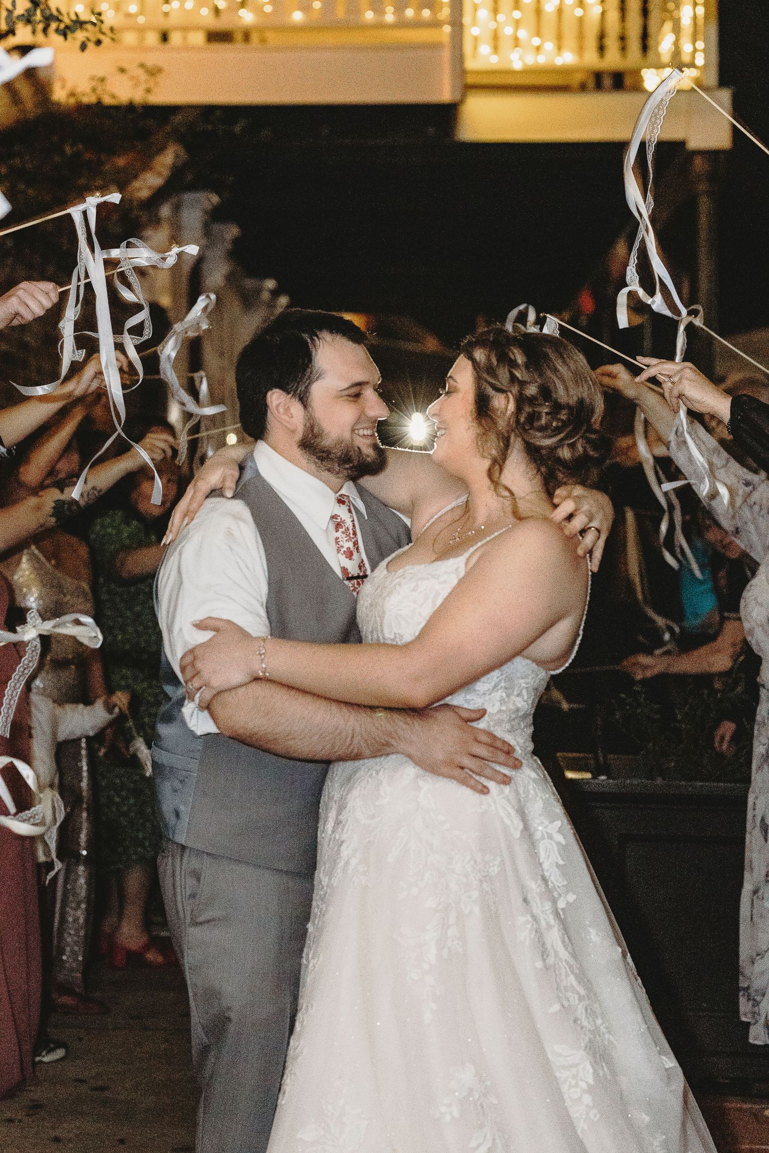 A newlywed couple shares their first dance surrounded by ribbon wands and twinkling lights.
