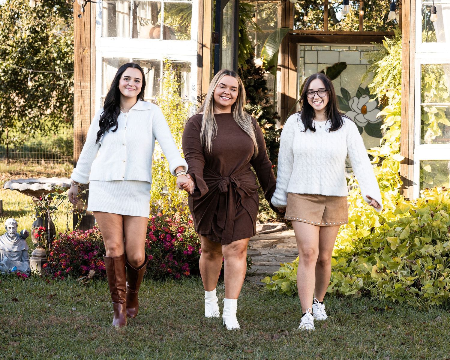 A group of people in casual attire walk together through a garden setting during golden hour lighting.