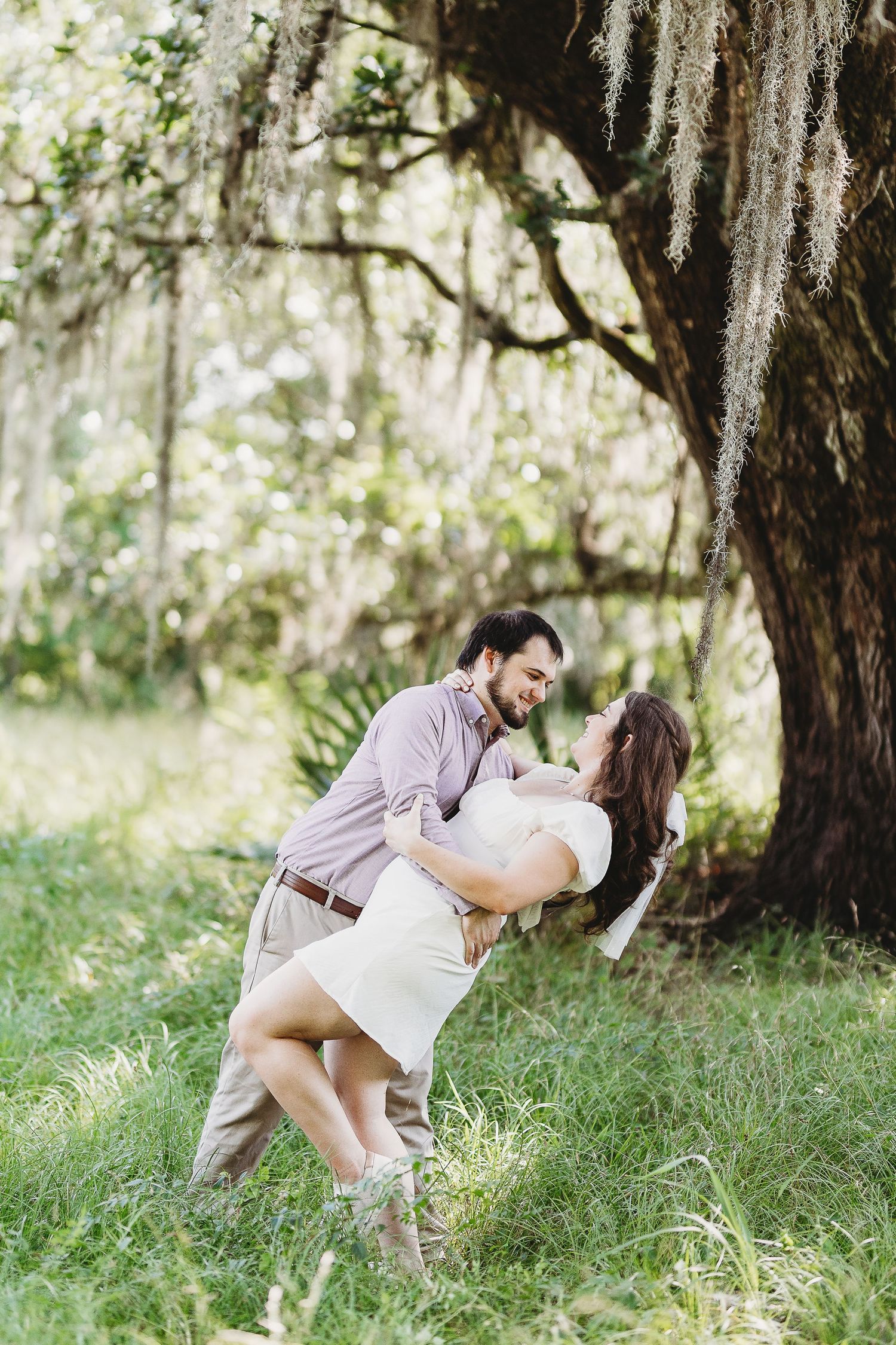 A romantic dip pose captured in a dreamy outdoor setting with Spanish moss hanging from trees.