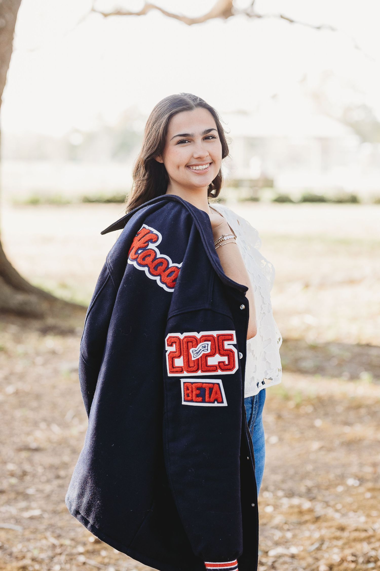Person wearing varsity jacket poses during outdoor portrait session.