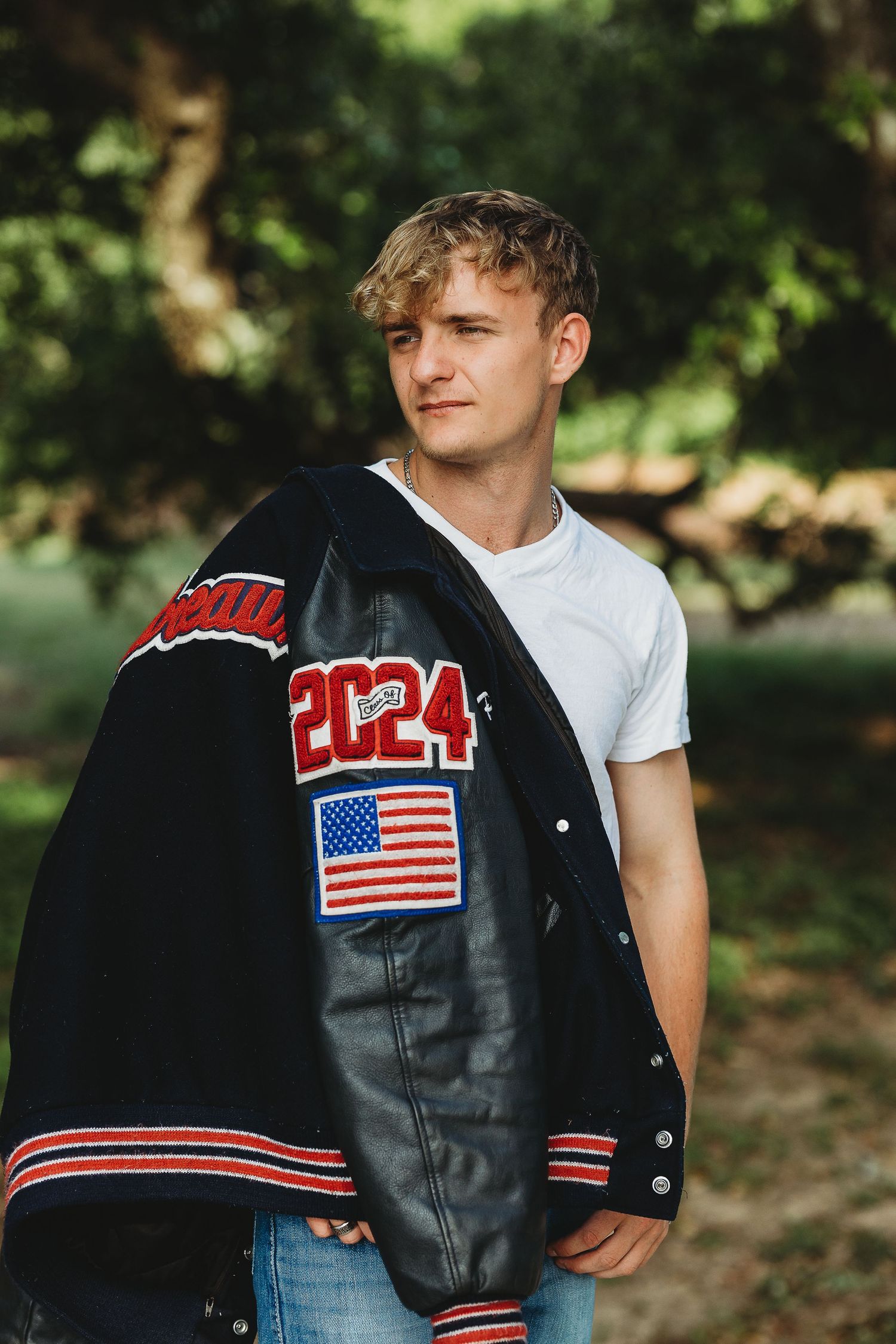 Black varsity jacket with American flag patch displayed against natural outdoor setting.