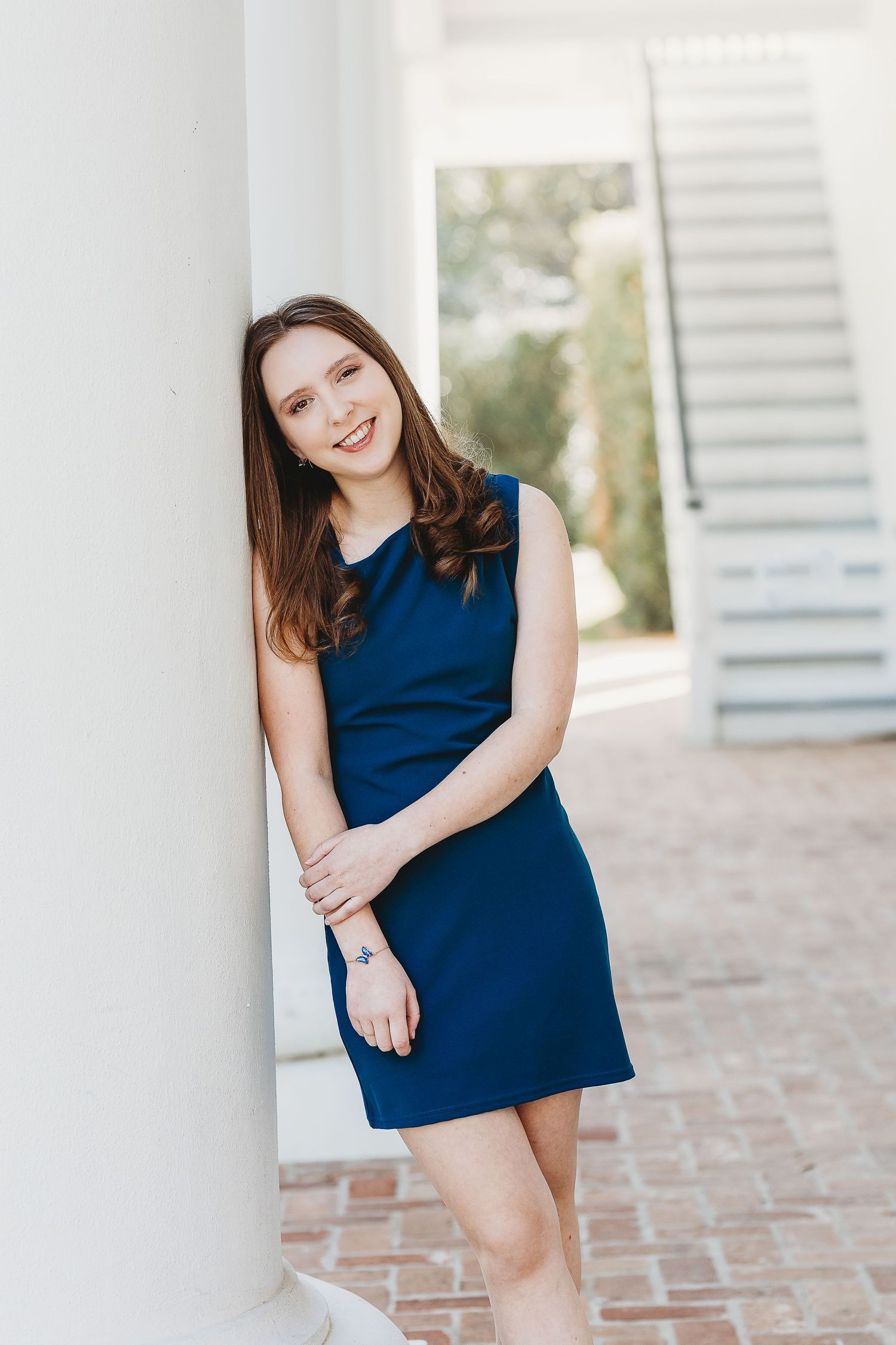 Portrait in navy blue dress leaning against white column with architectural details.