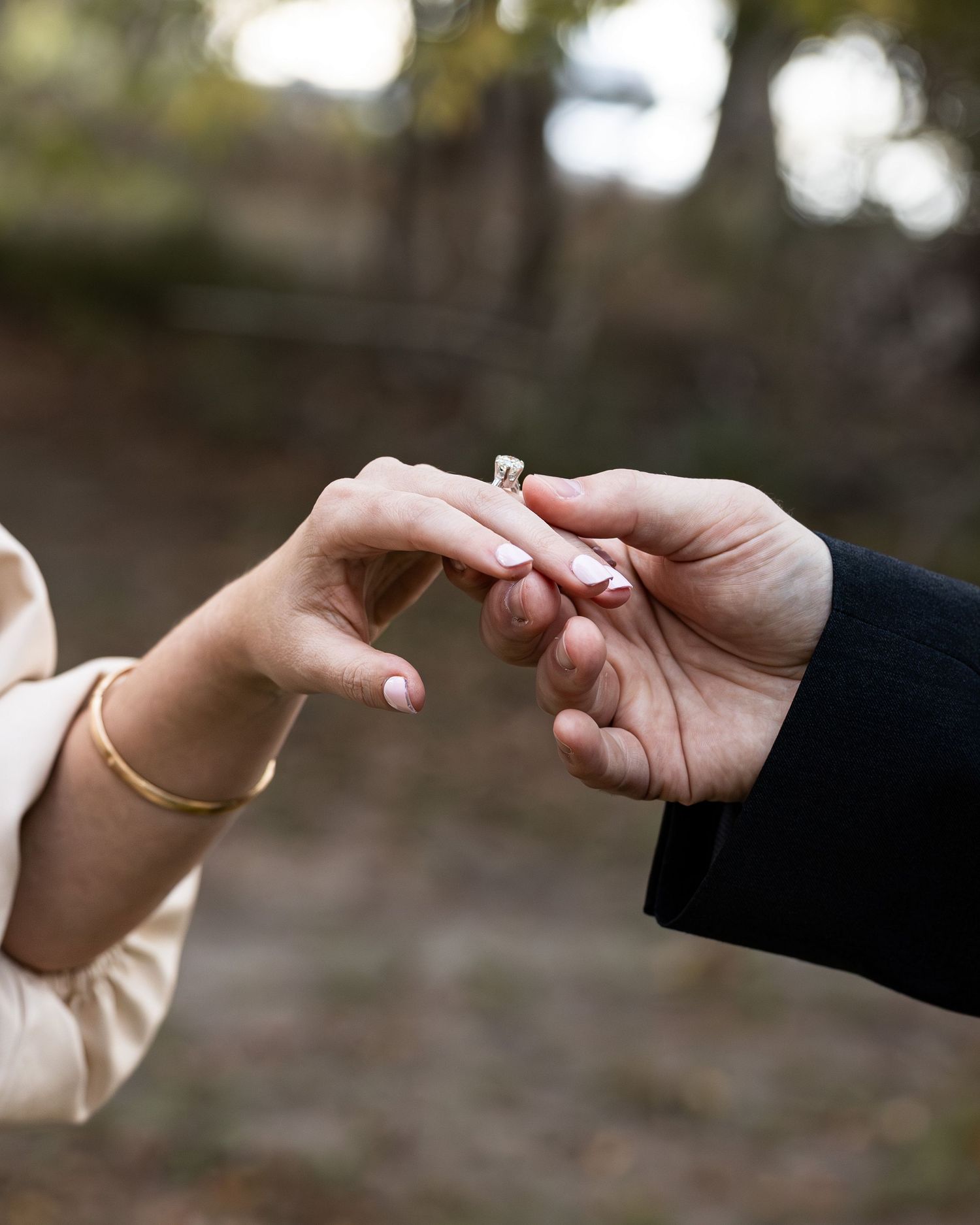 Close-up shot of two hands exchanging a wedding ring during a romantic outdoor ceremony.