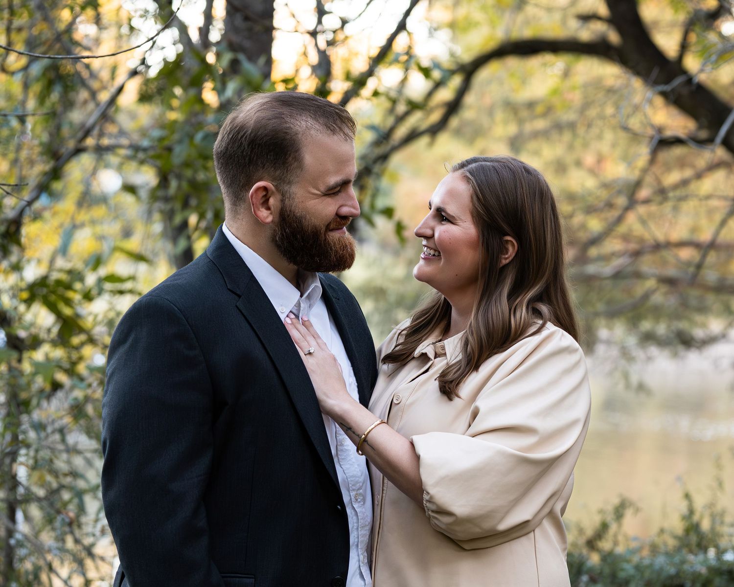 Couple embracing tenderly outdoors with fall foliage and a lake creating a romantic natural backdrop.