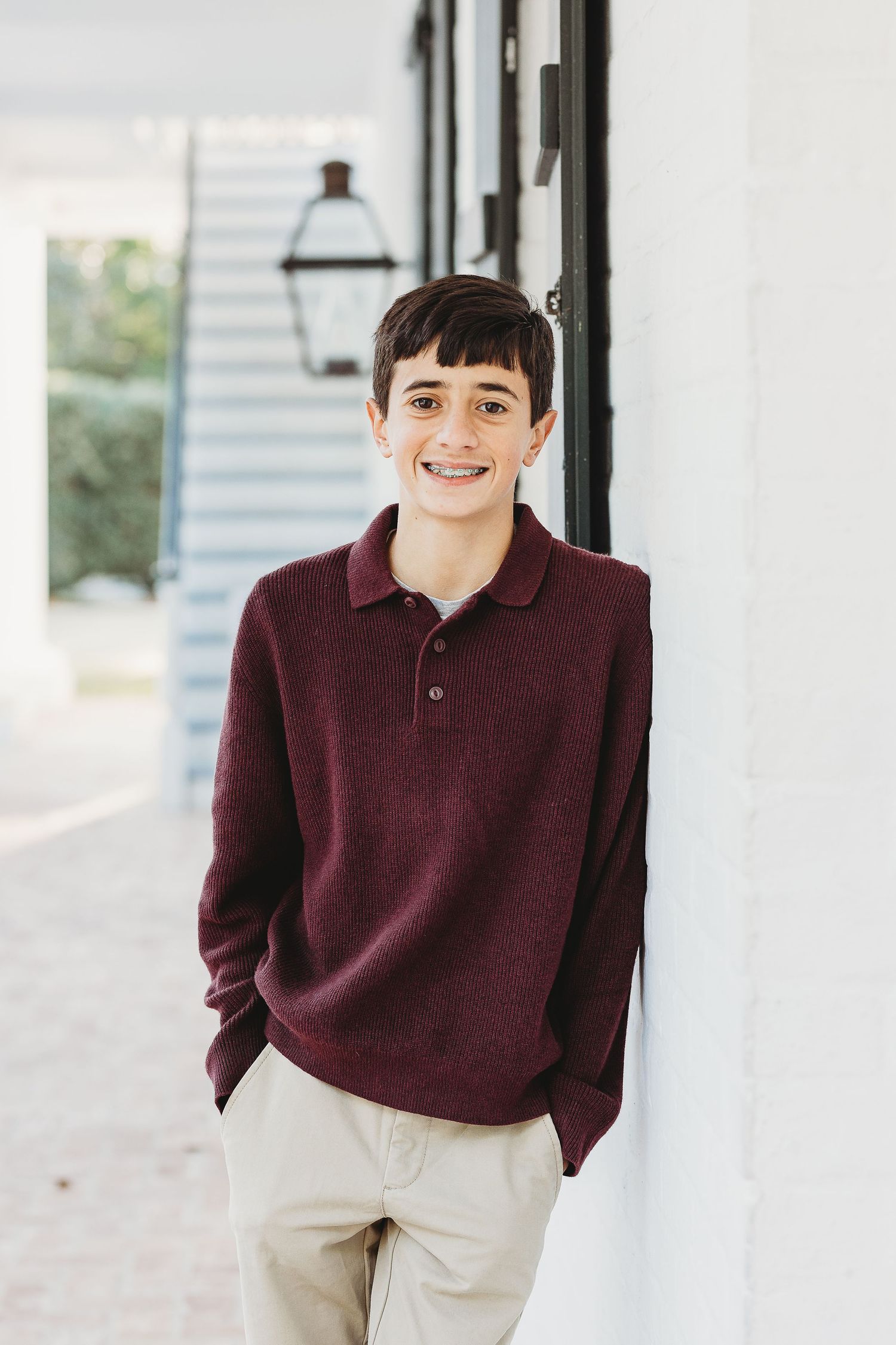 Young person in burgundy sweater and khaki pants poses confidently against white columns.