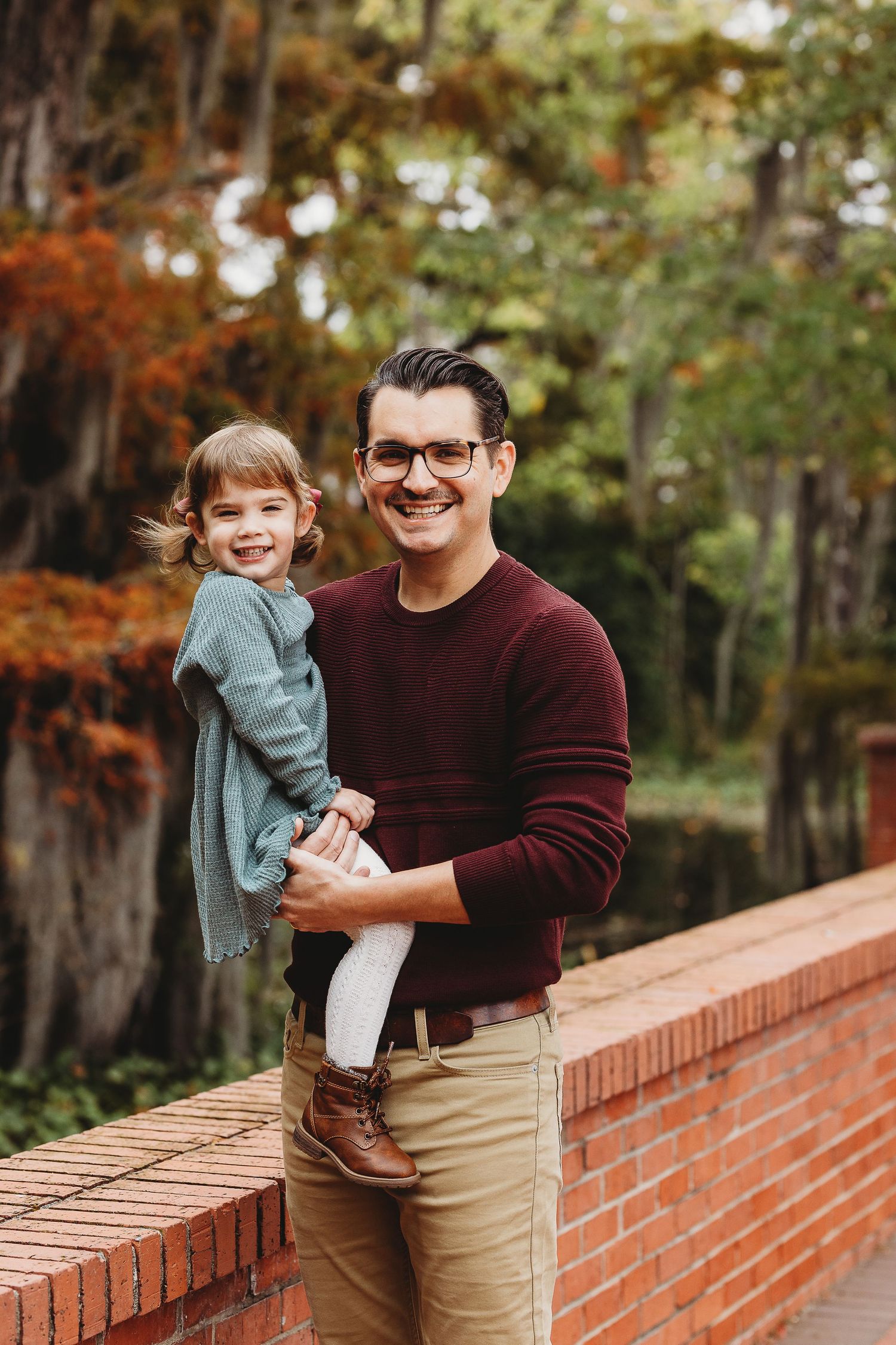 Autumn family portraits on a brick wall with warm fall colors in the background.