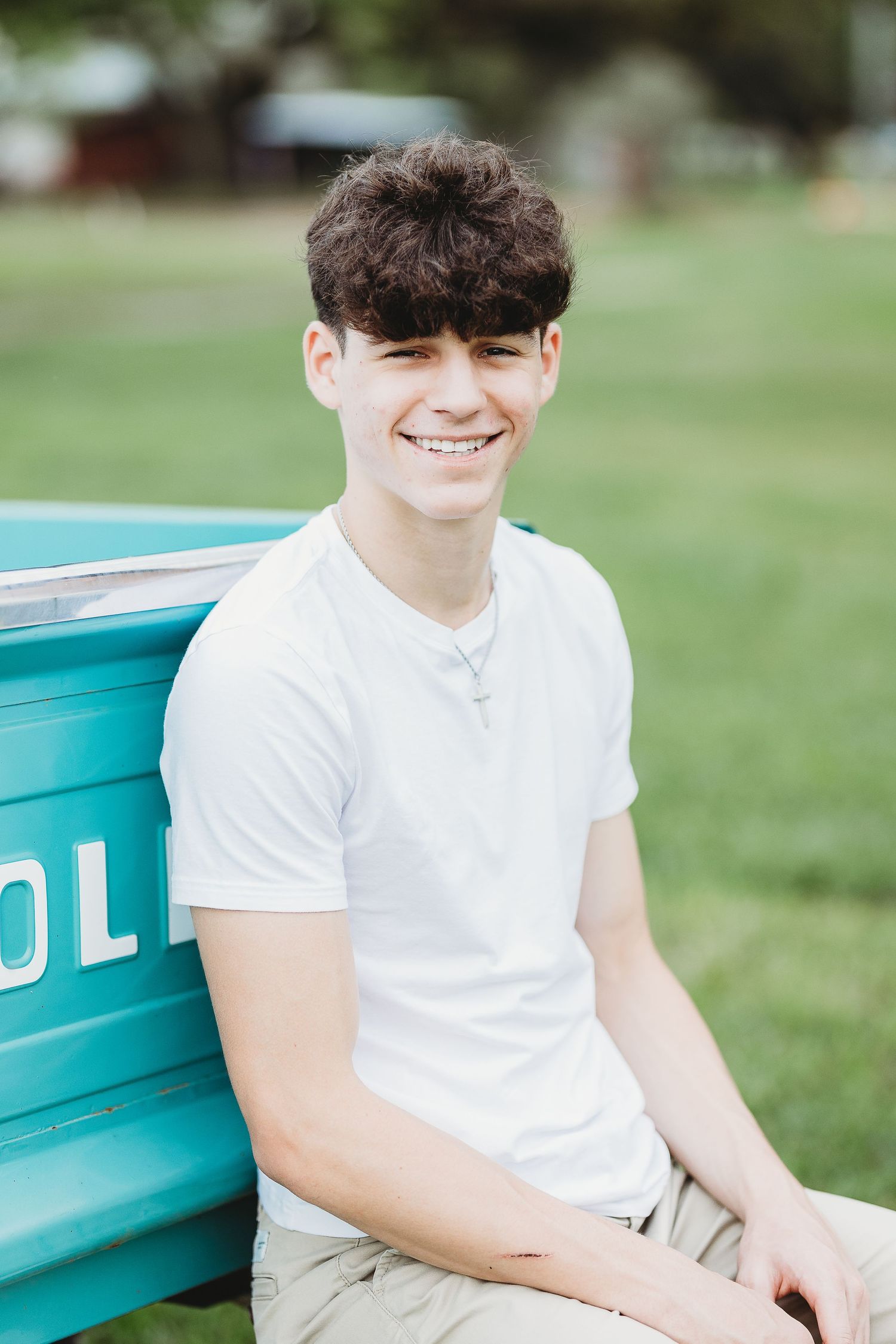 Person in white t-shirt sits casually against turquoise vintage truck bed in sunny outdoor setting.