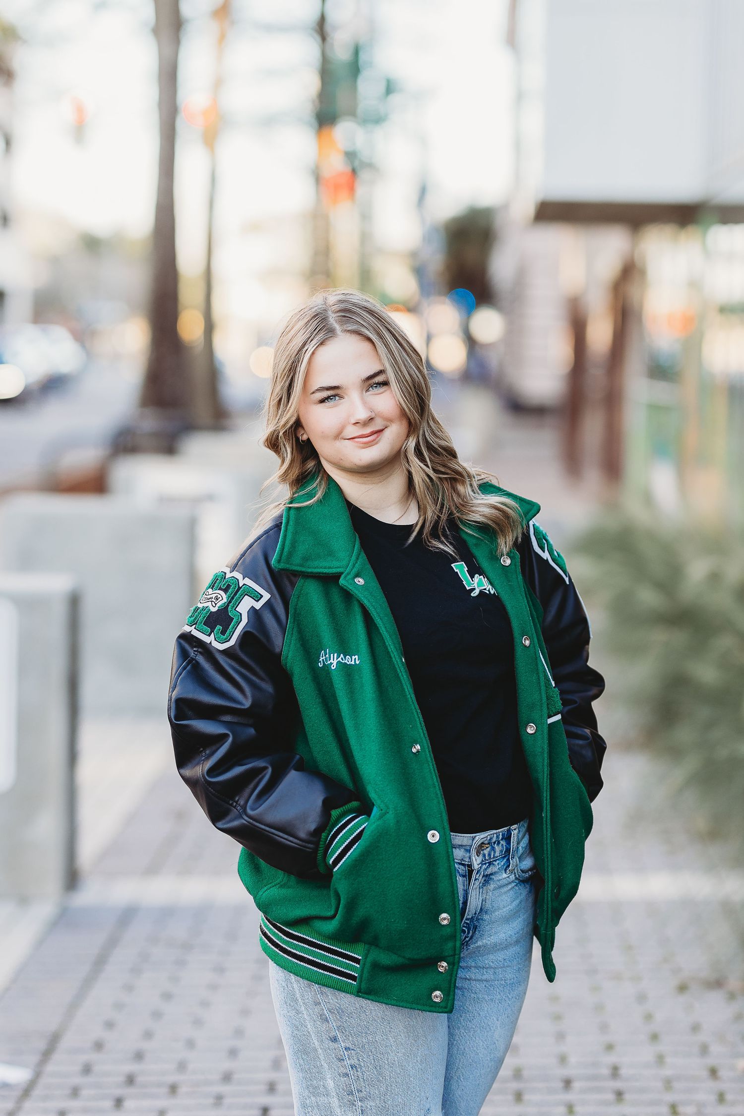 Green and black varsity jacket styled with light denim in urban setting.