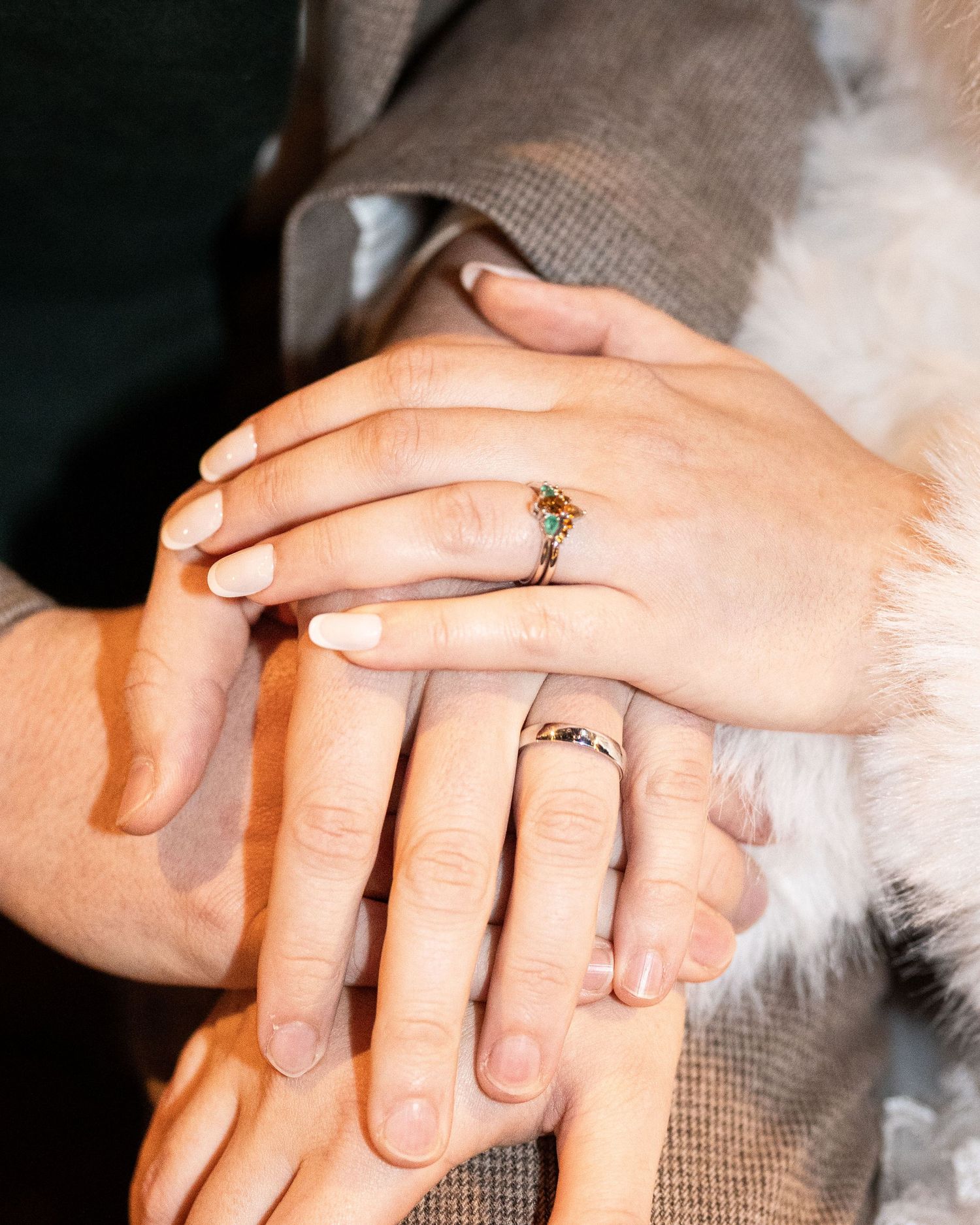 Close-up sequence of hands placing engagement rings on fingers against a soft gray background.