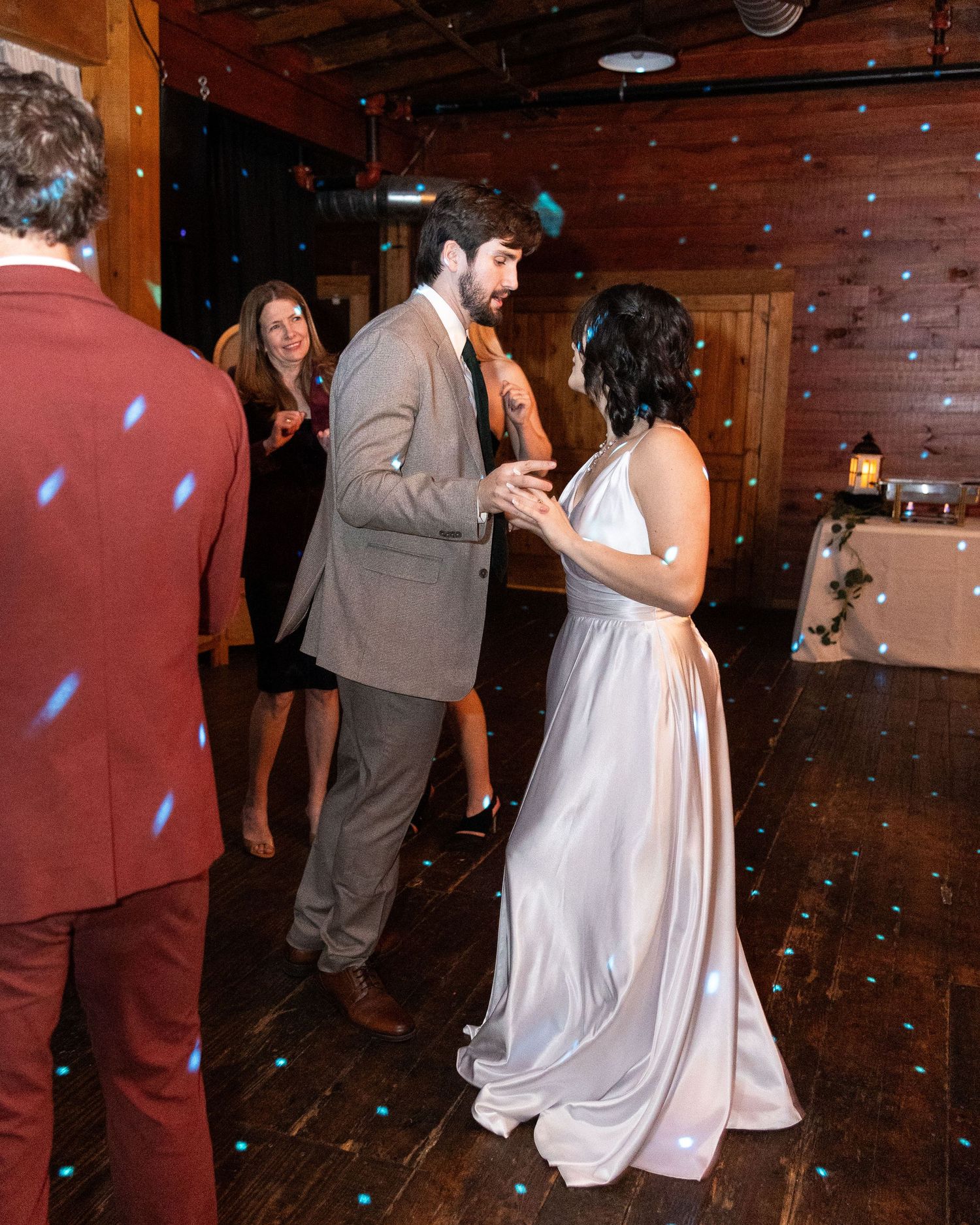 Wedding guests dance in a rustic wooden venue with blue confetti floating through the air.