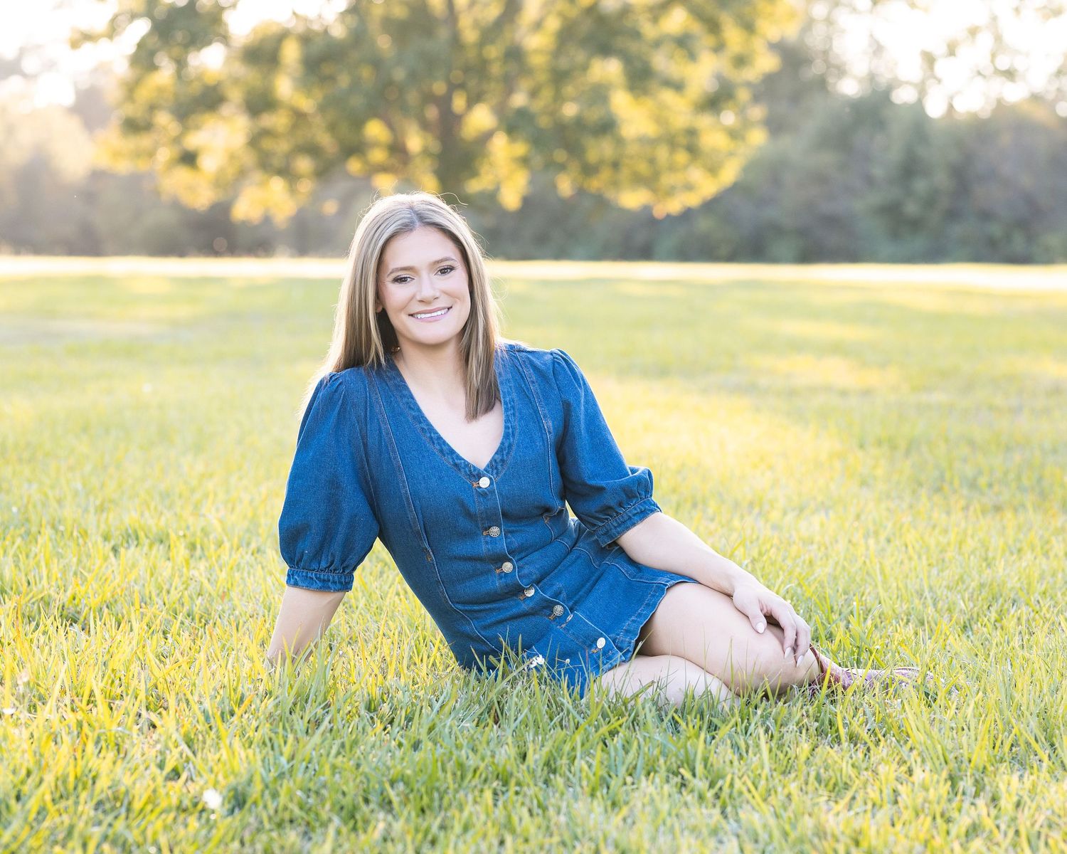 Person in blue dress lounges in golden sunlit grass field during sunset.