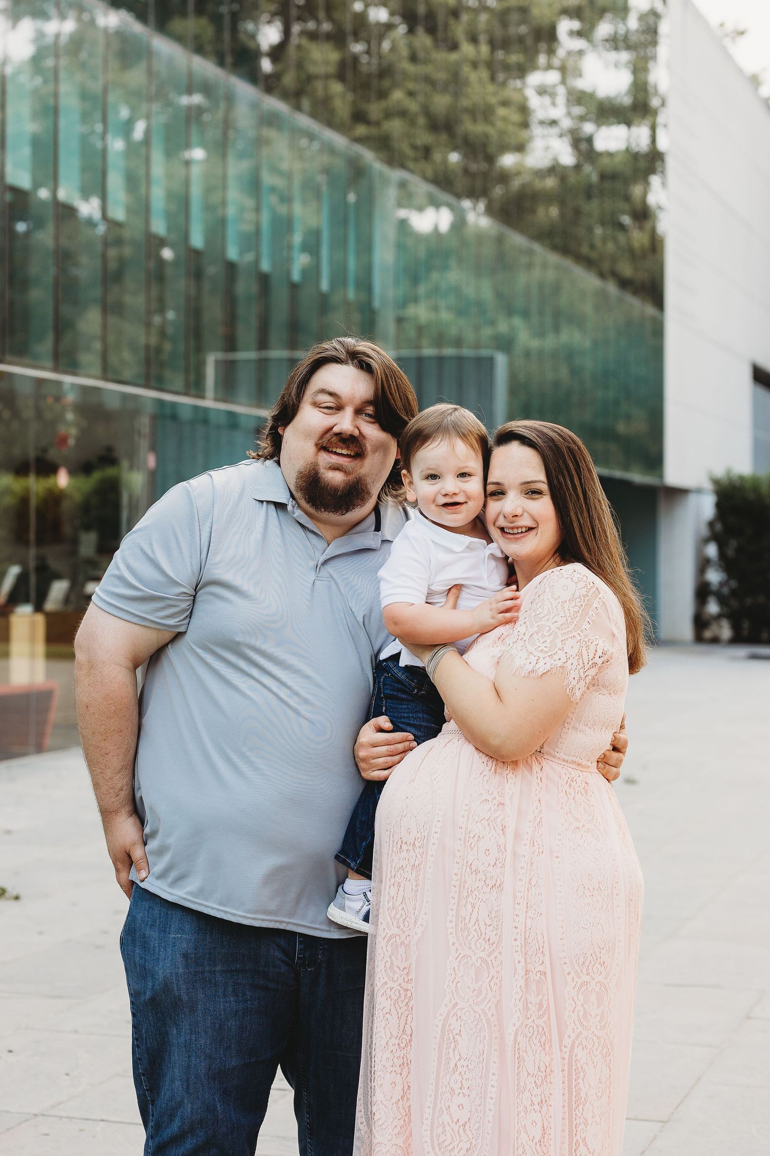 Family dressed in soft pastels posing against modern glass building exterior.