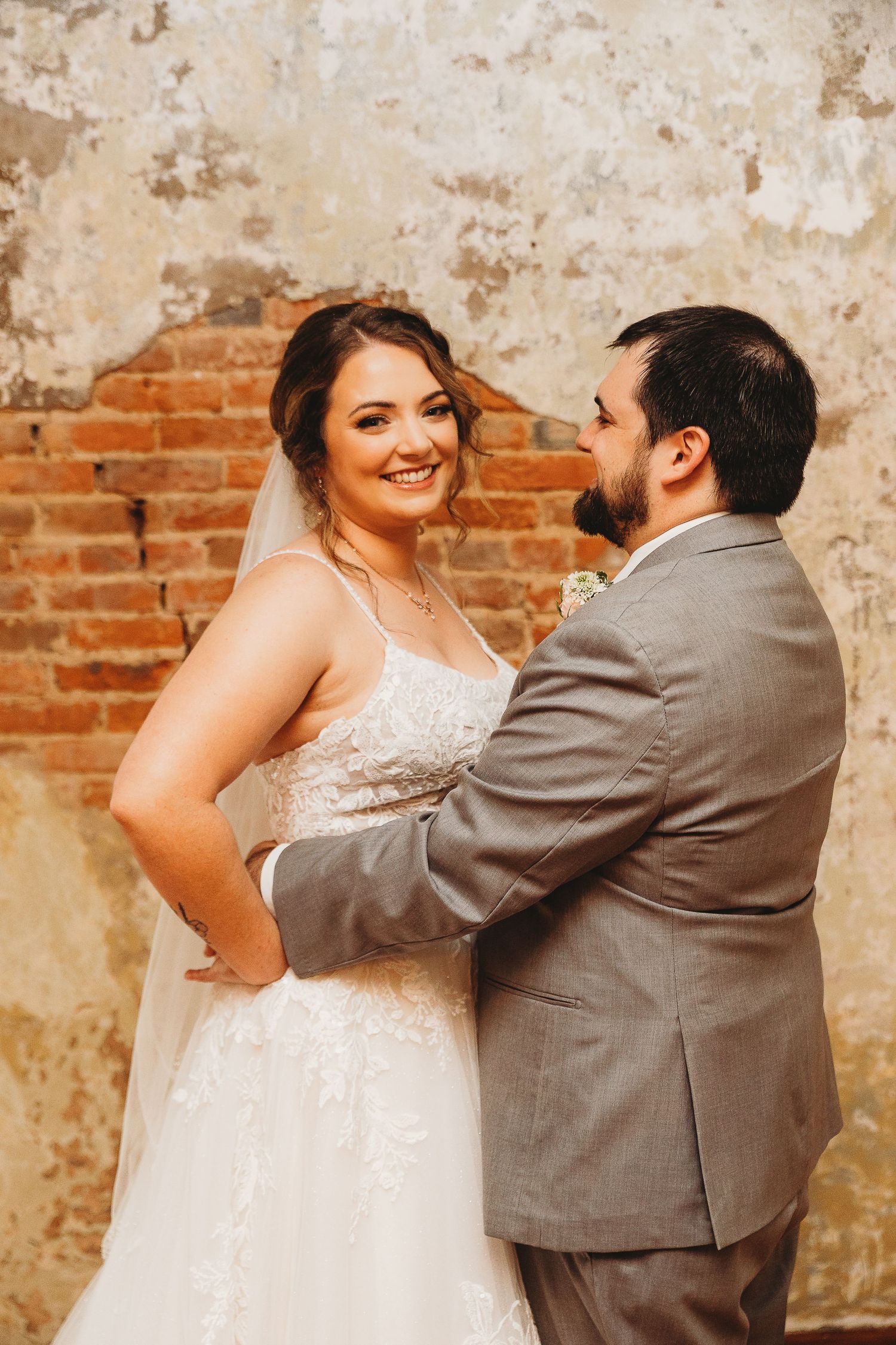 Candid wedding portraits showing joyful moments against an industrial brick backdrop.