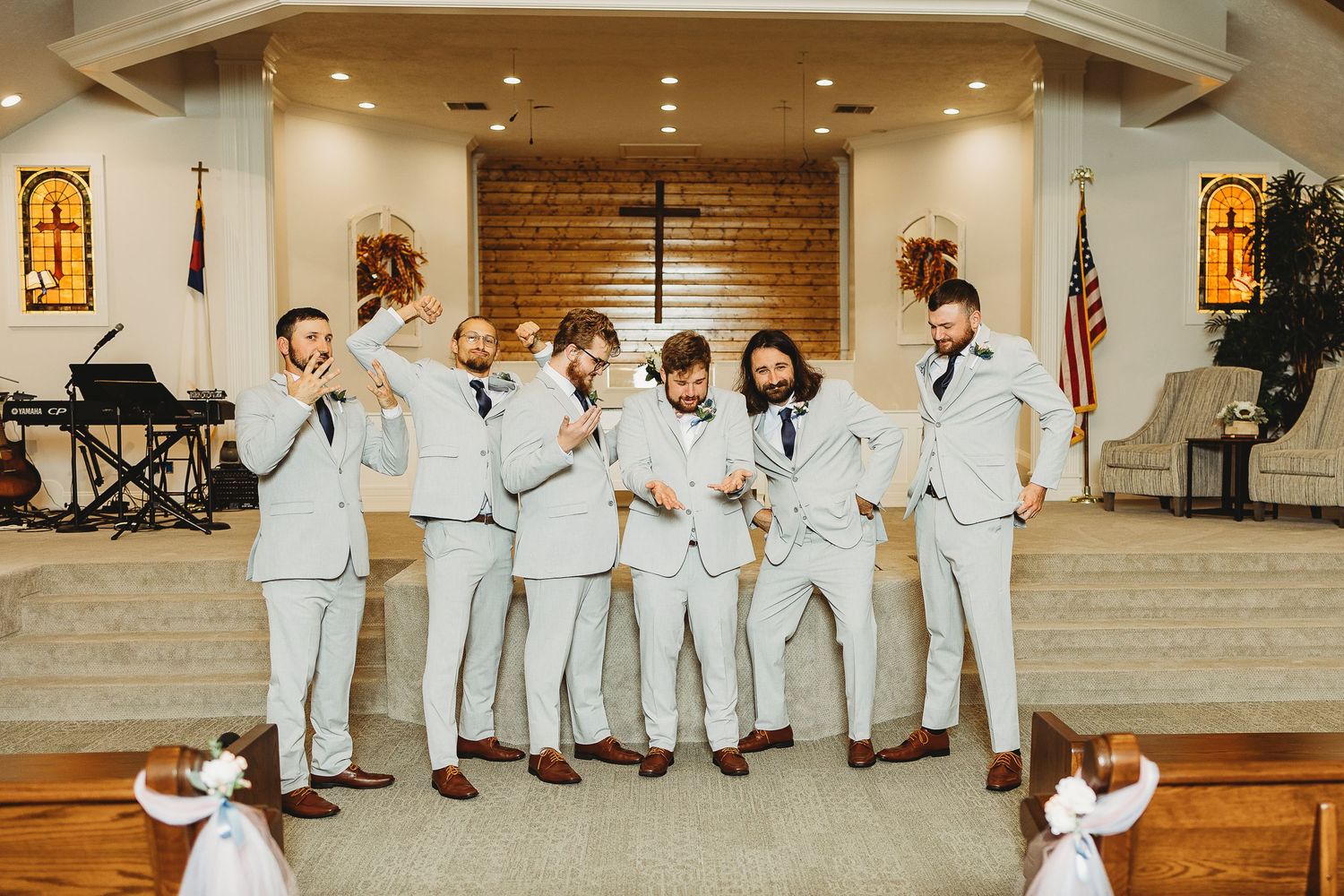 Groomsmen in light colored suits pose playfully on church steps during wedding celebrations.